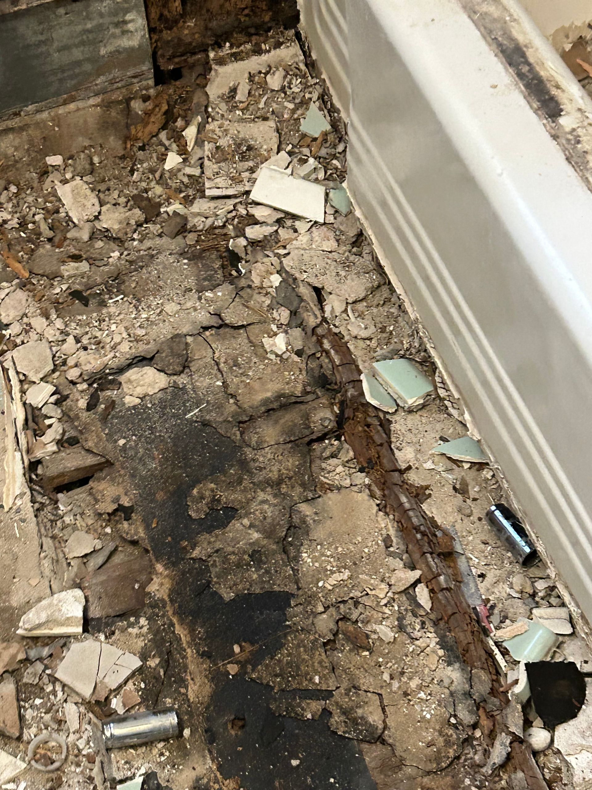 Bathroom floor damage with broken tiles, exposed wood, and a partially visible bathtub.