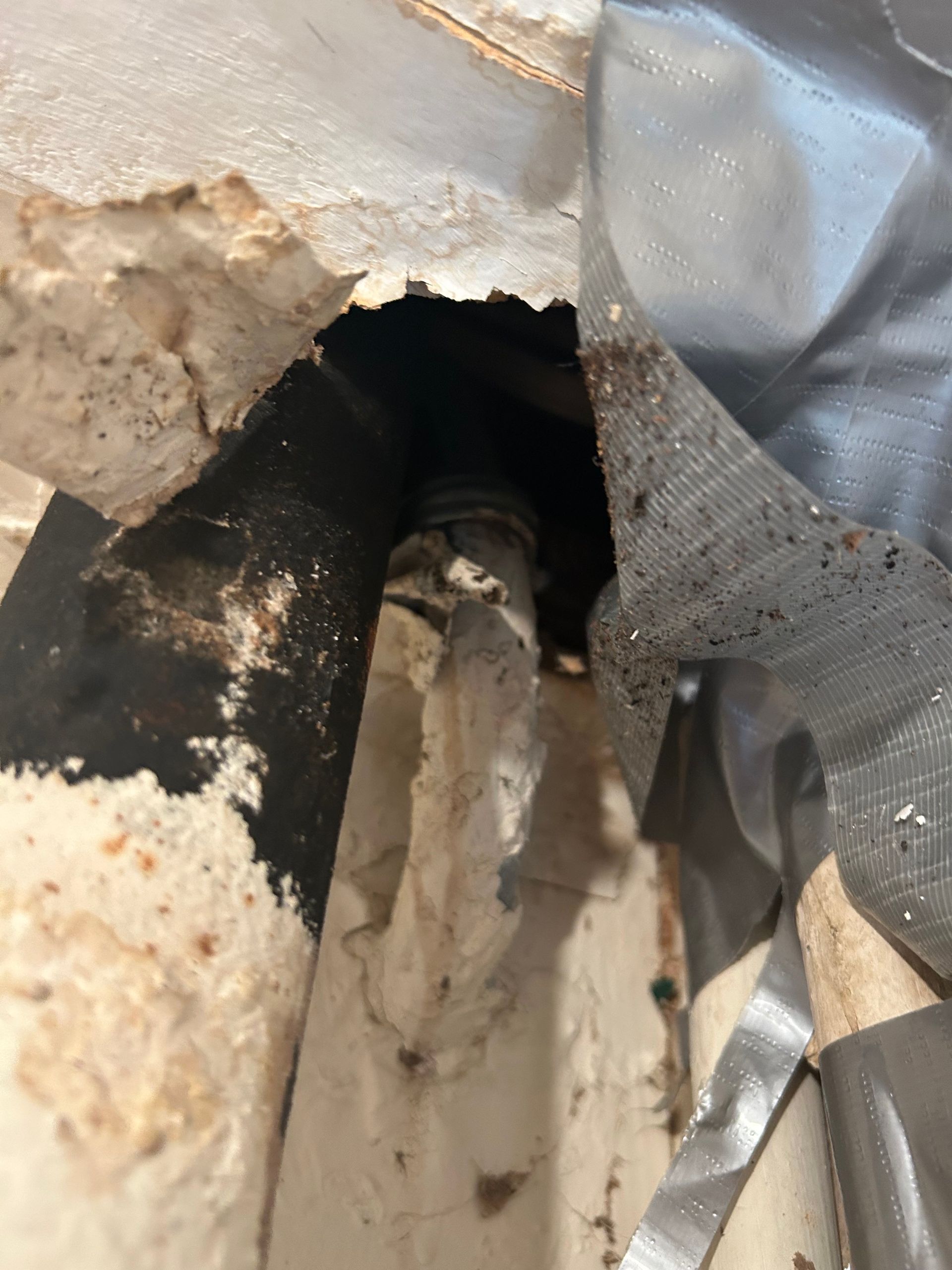 Hole in wall with damaged plaster and duct tape. A dark pipe is visible inside the hole.