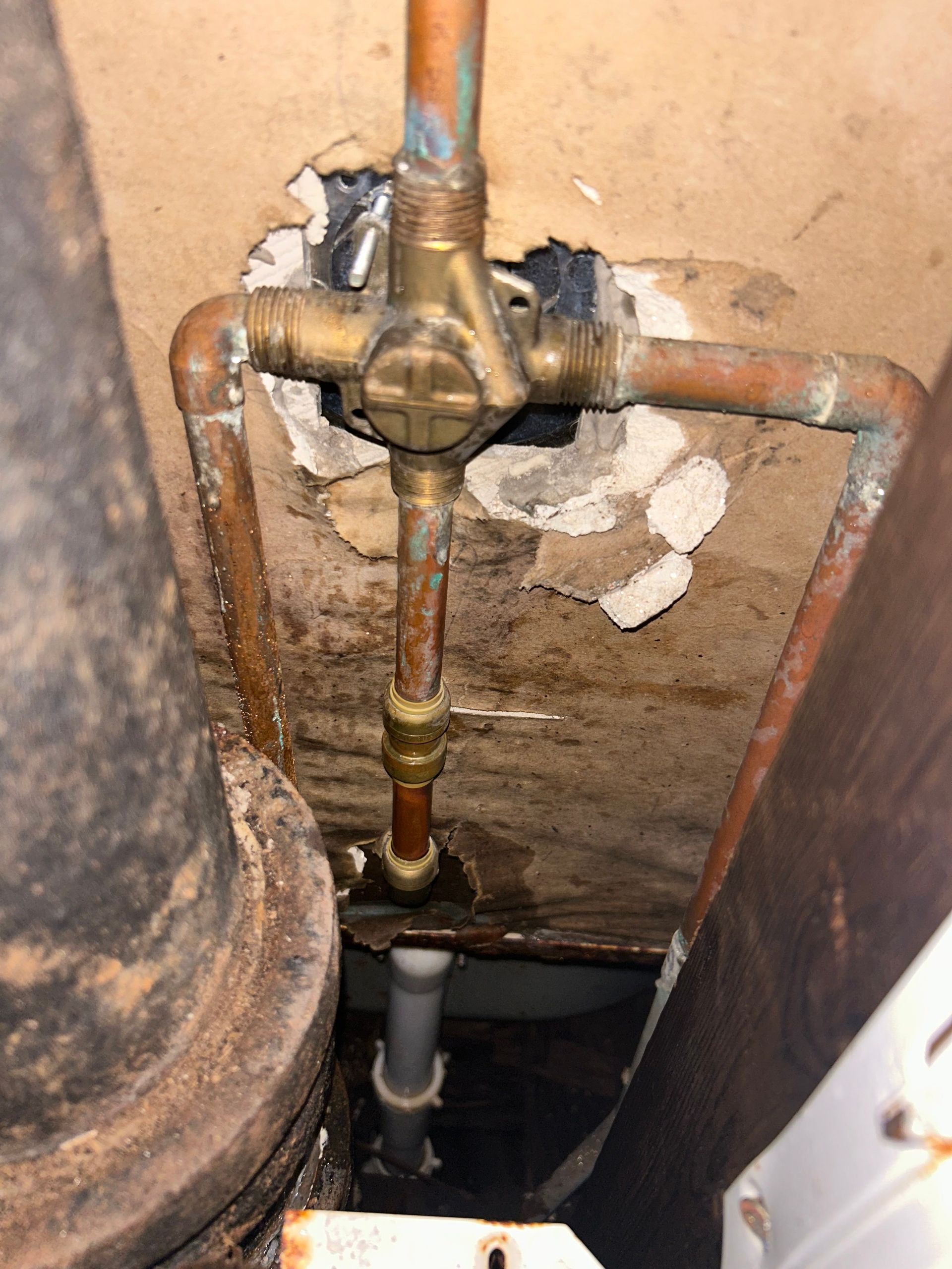 Copper pipes connected to a brass valve, with a water stain on the wall.