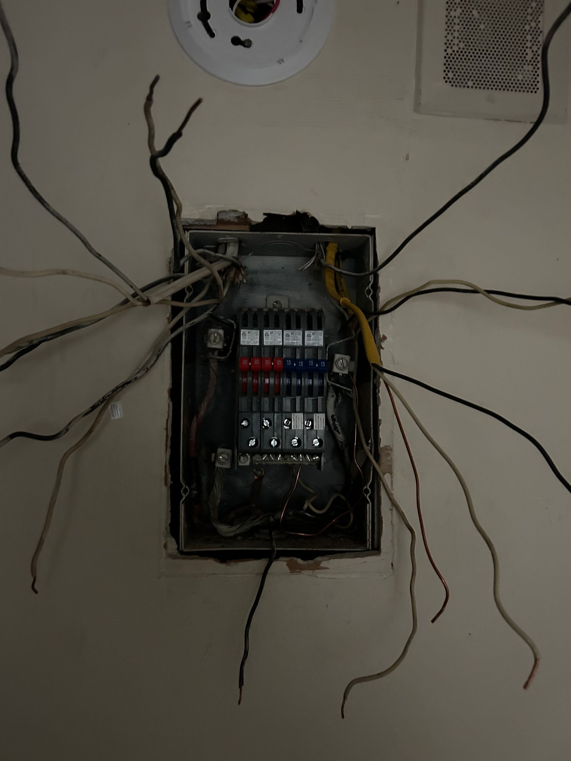 Open electrical panel with numerous wires protruding from a wall.