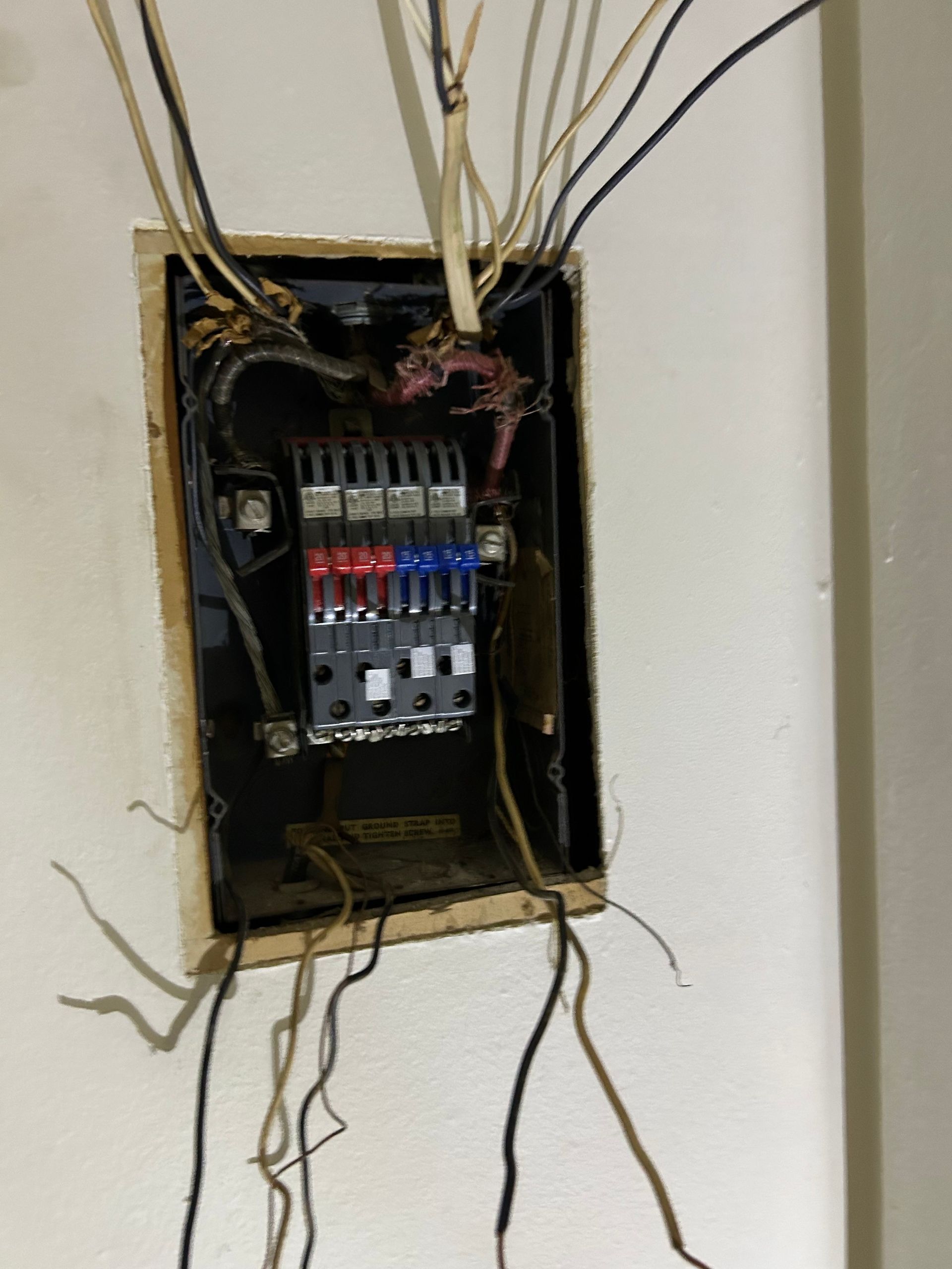 Electrical panel with exposed wiring, mounted on a white wall.