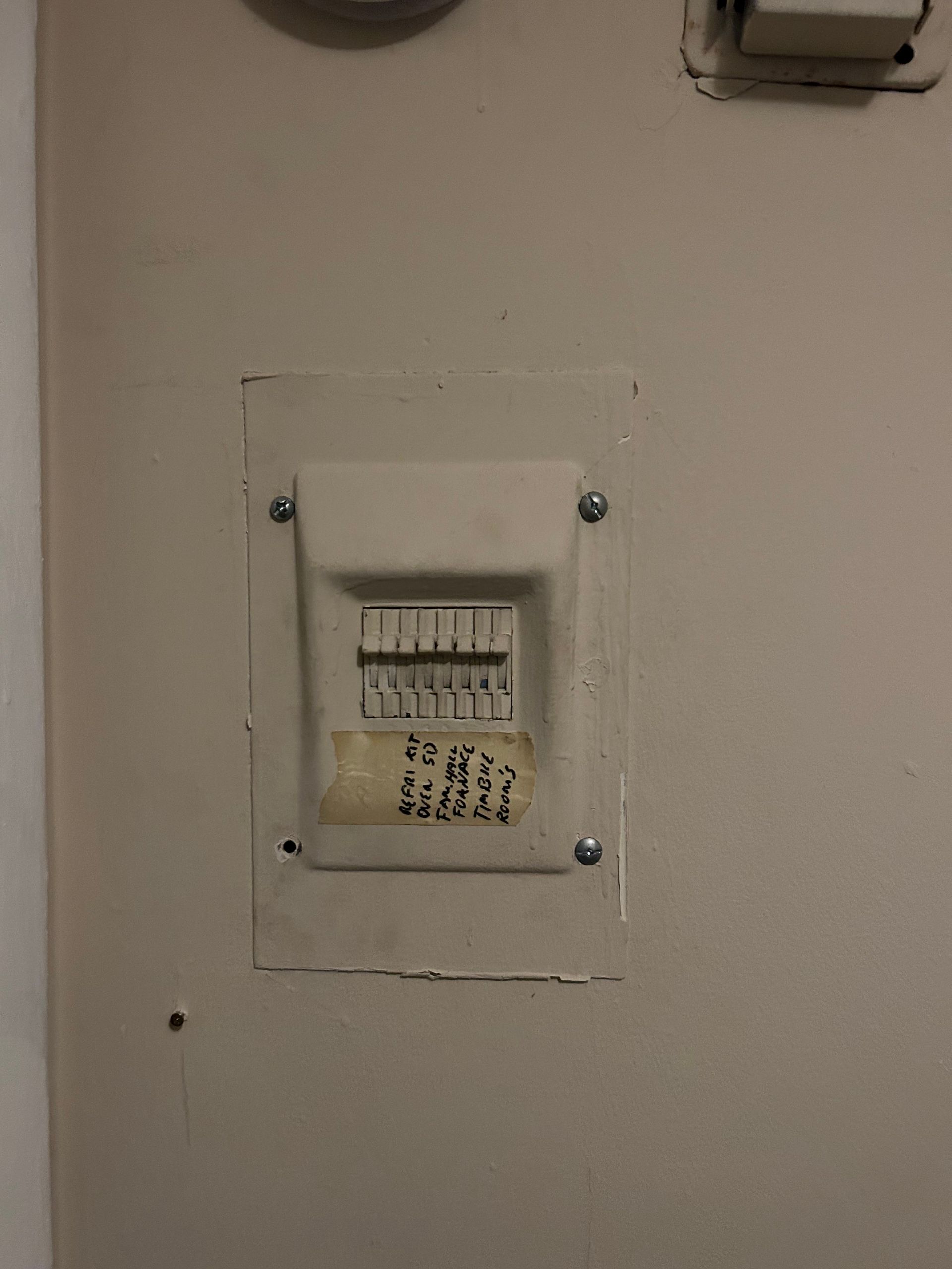 Small electrical breaker box with on/off switches mounted on a wall, with handwritten labels below.