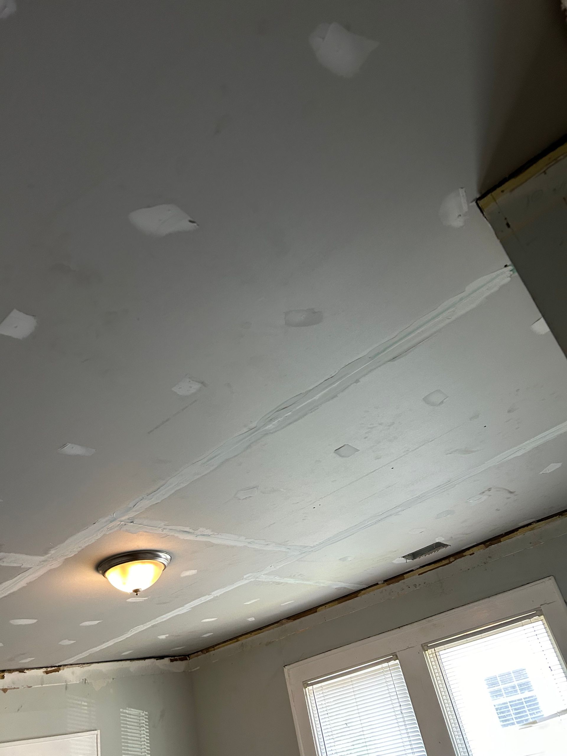 Ceiling drywall with taped seams and patches. Light fixture, partially framed window.
