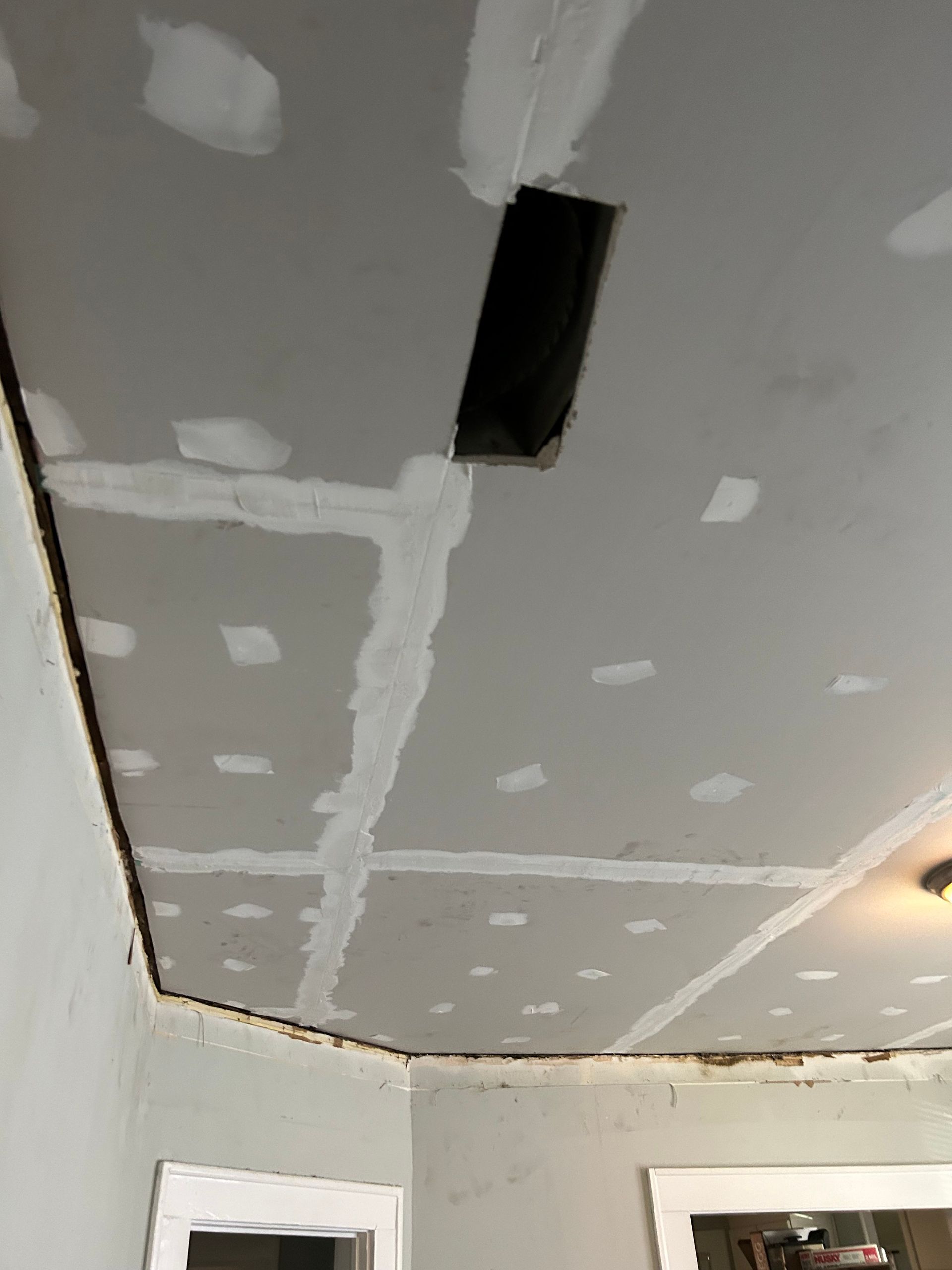 Drywall ceiling with mudded seams and vent. Partially constructed room with windows.