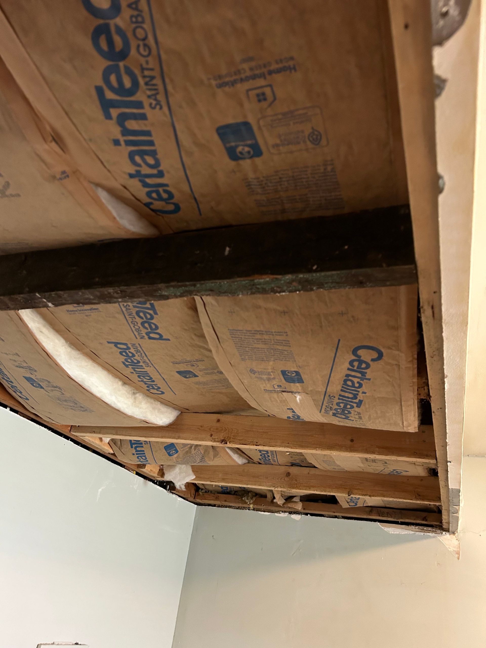 View of an exposed ceiling with insulation and wooden beams, highlighting construction details.