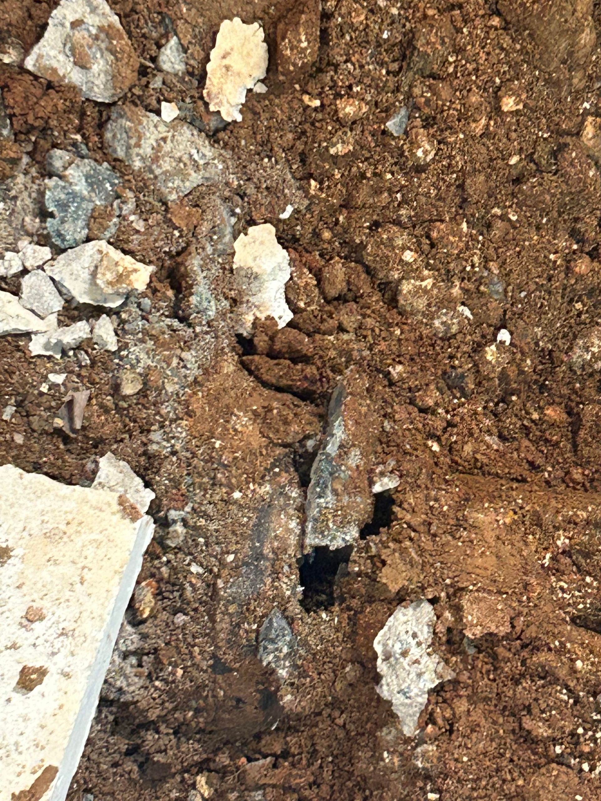 Hole in the ground surrounded by dirt and chunks of light-colored concrete.