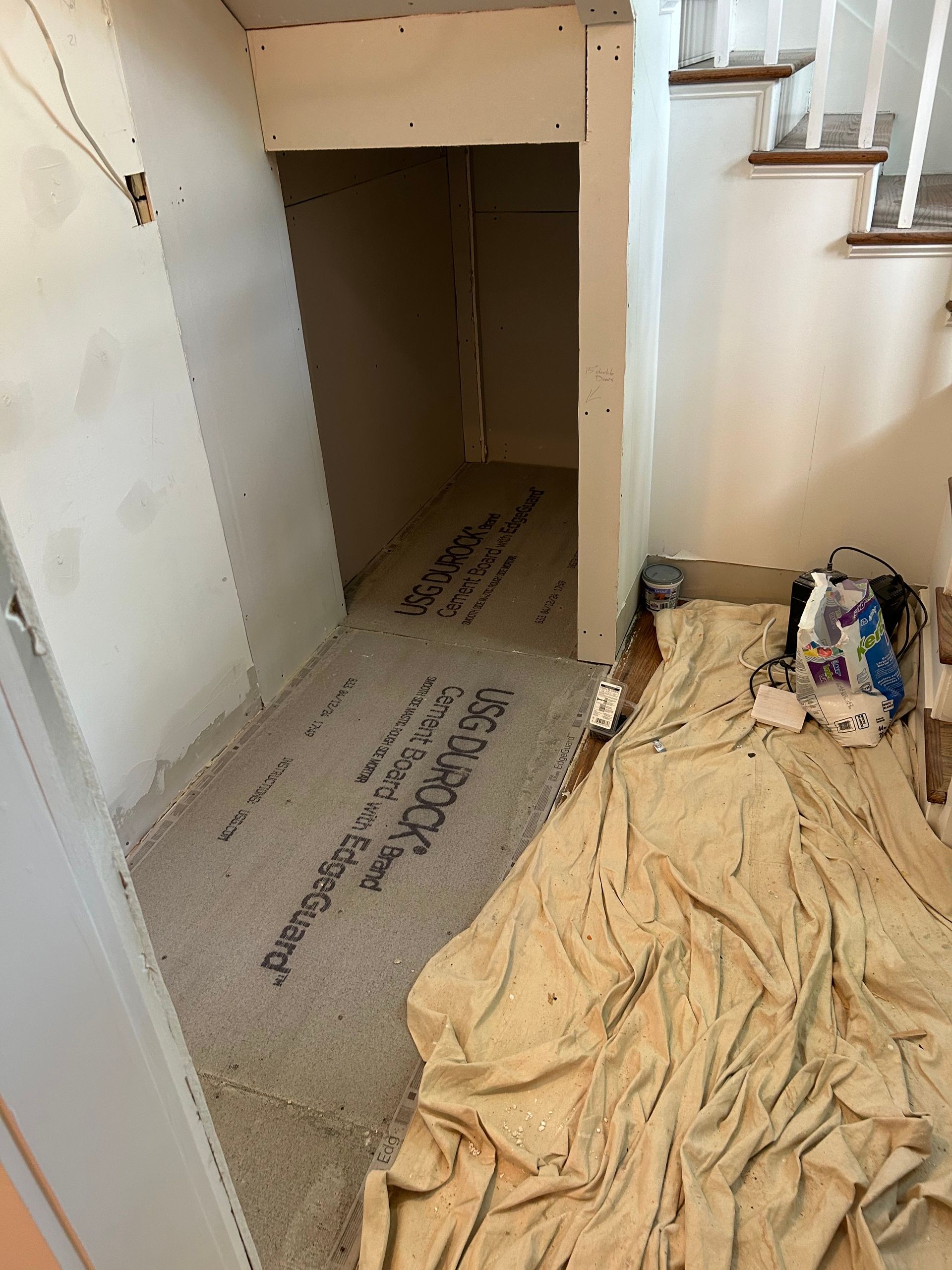 Construction in progress under stairs: drywall, flooring, drop cloth, staircase, unfinished room.