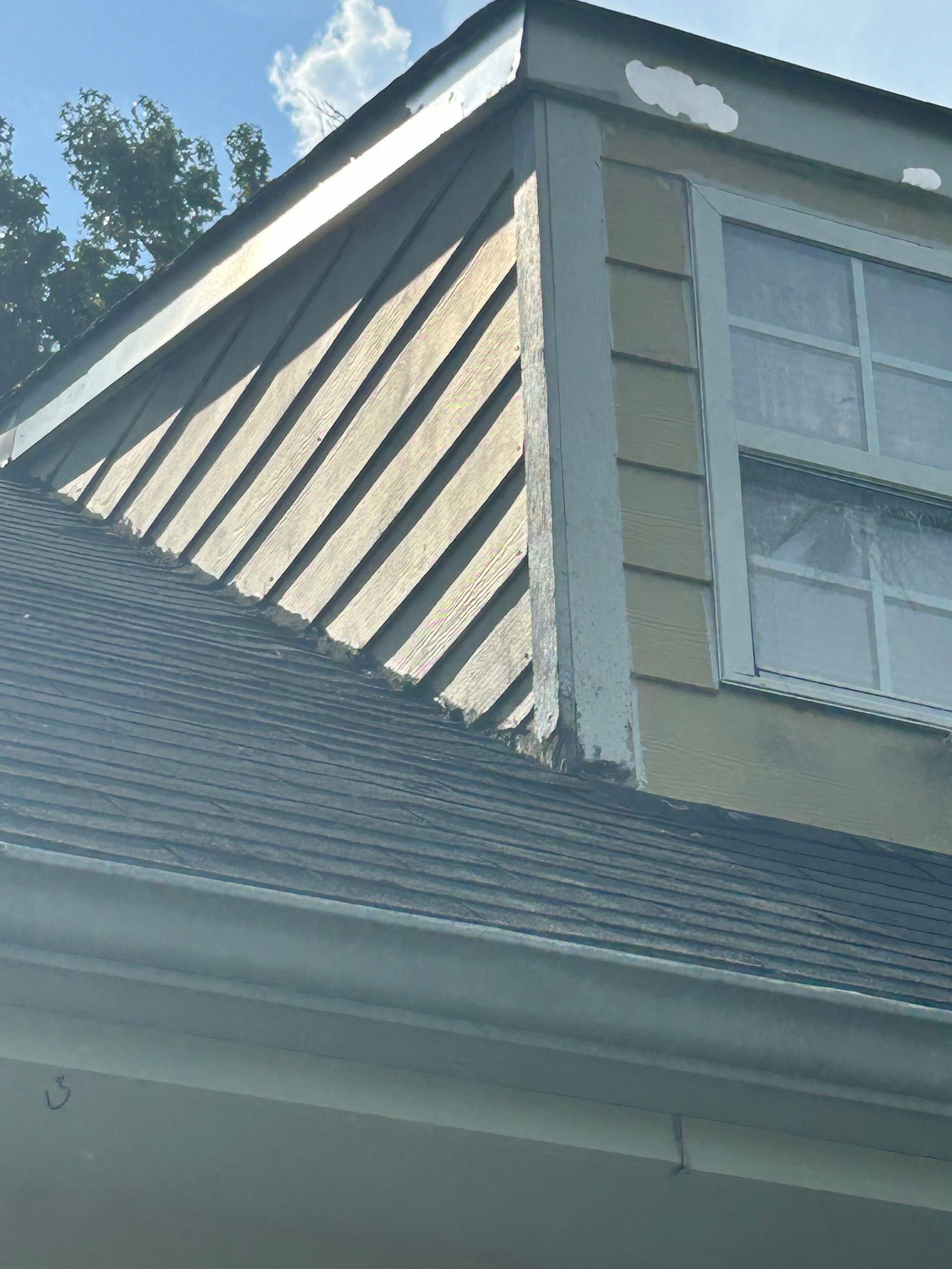 Angled view of a house roof with metal siding, window, and gutter under a blue sky.