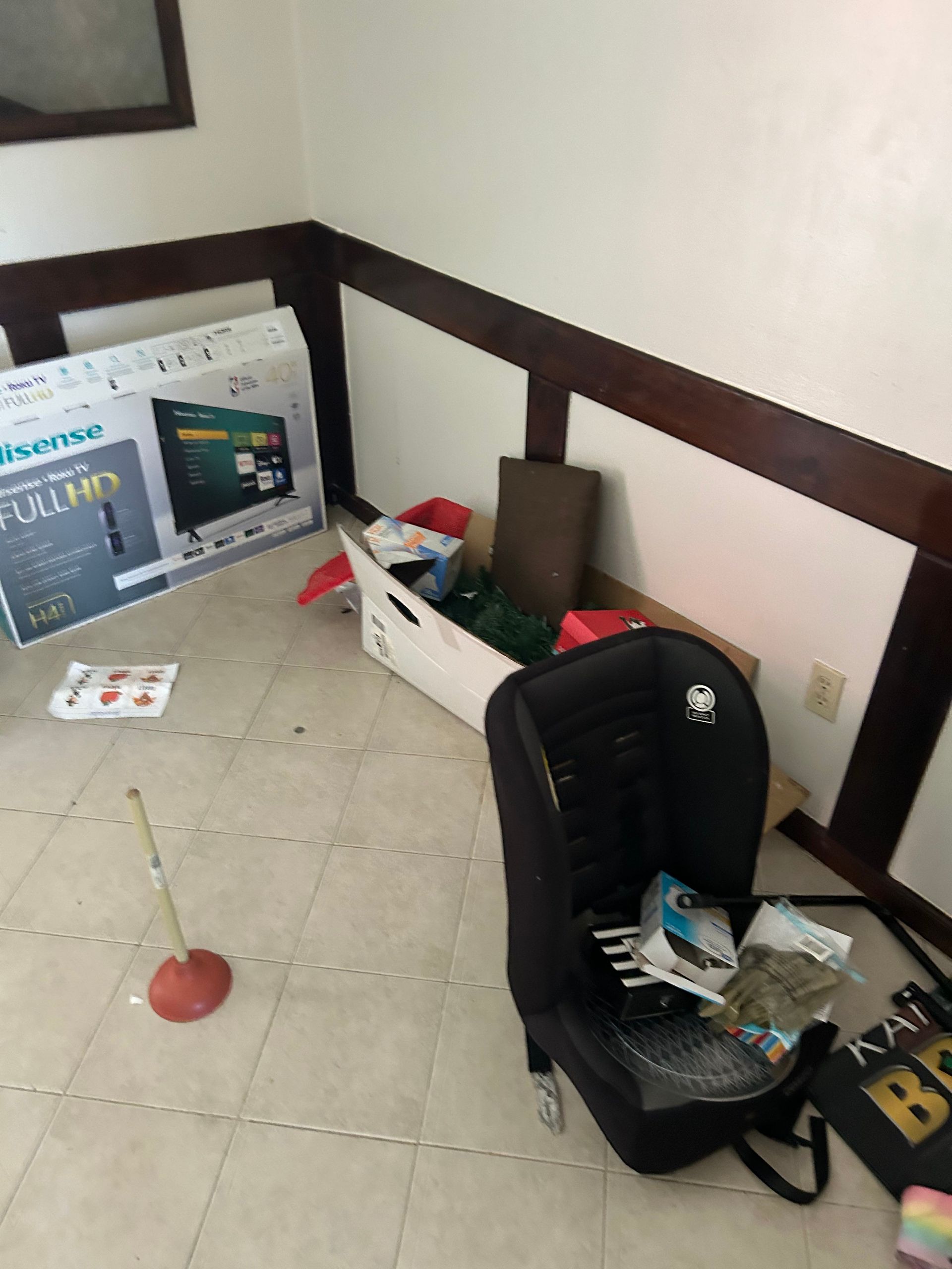 Corner of room with boxes, a chair, and a TV box. Brown trim and off-white walls and floor.