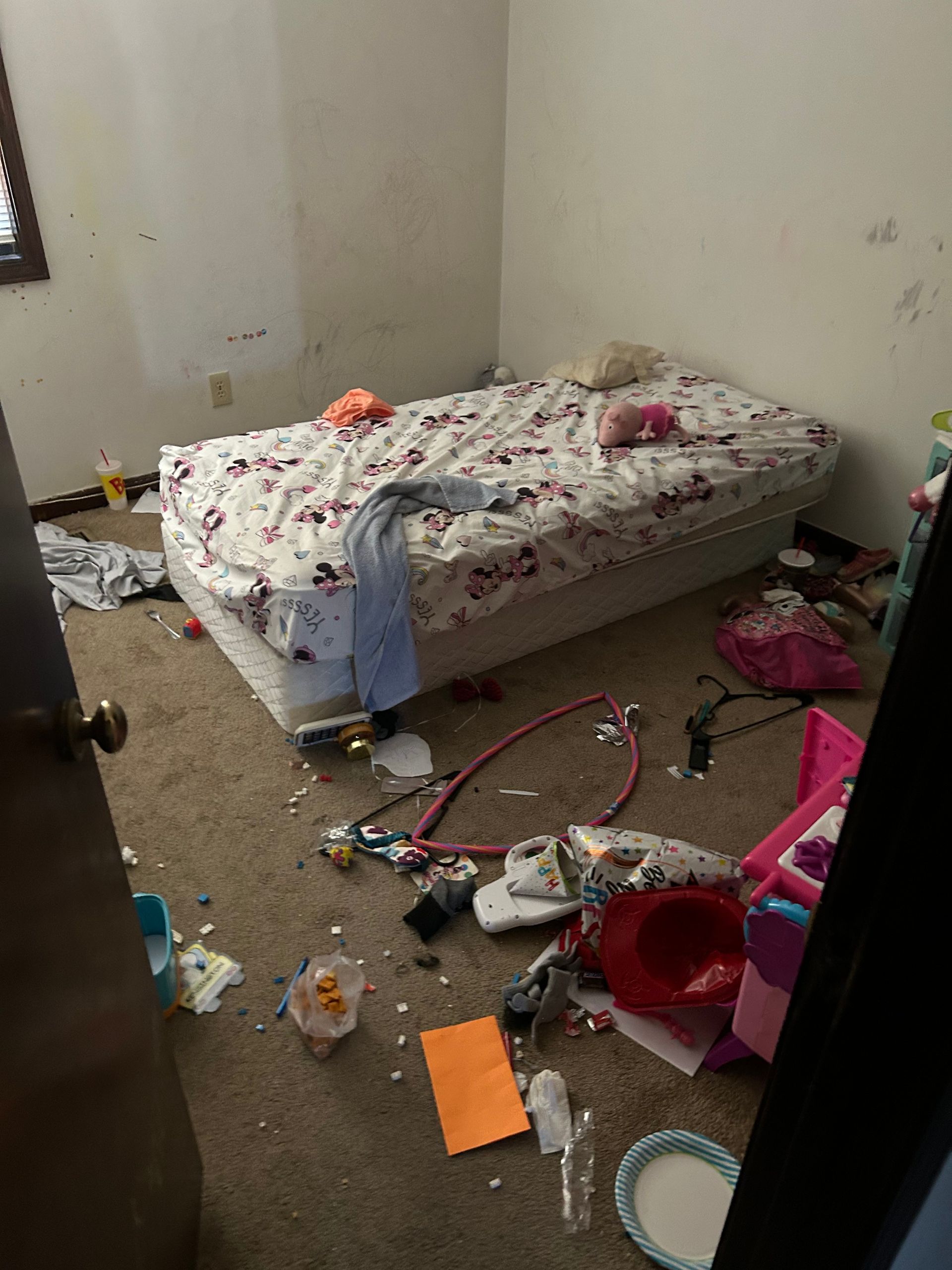 Messy bedroom with unmade bed, scattered toys, and trash on the floor.