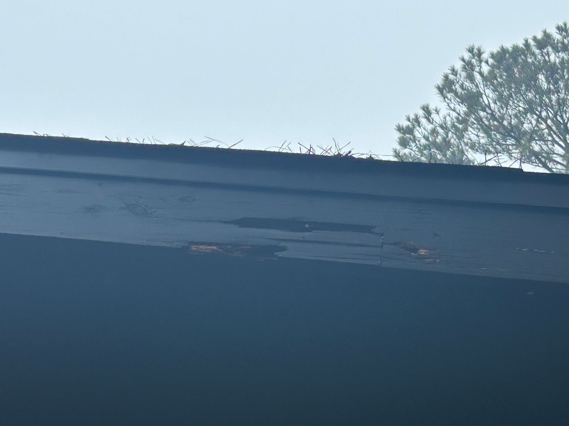 Dark roof with a damaged section; hazy sky and tree in background.