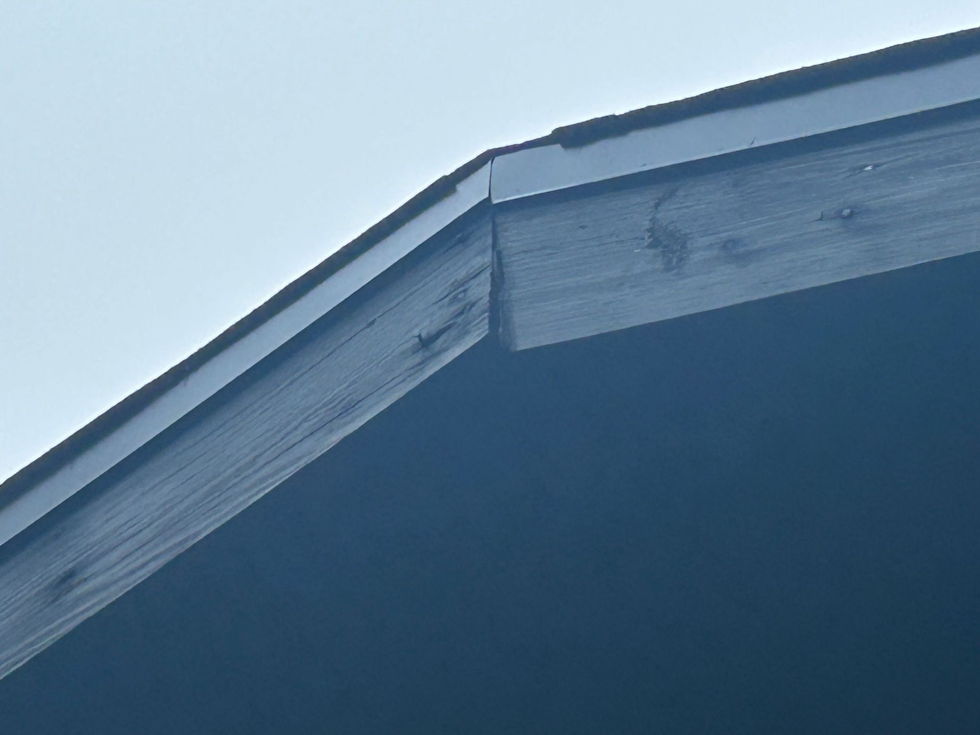 Close-up of a dark wooden roof edge, with a blue-gray sky in the background.