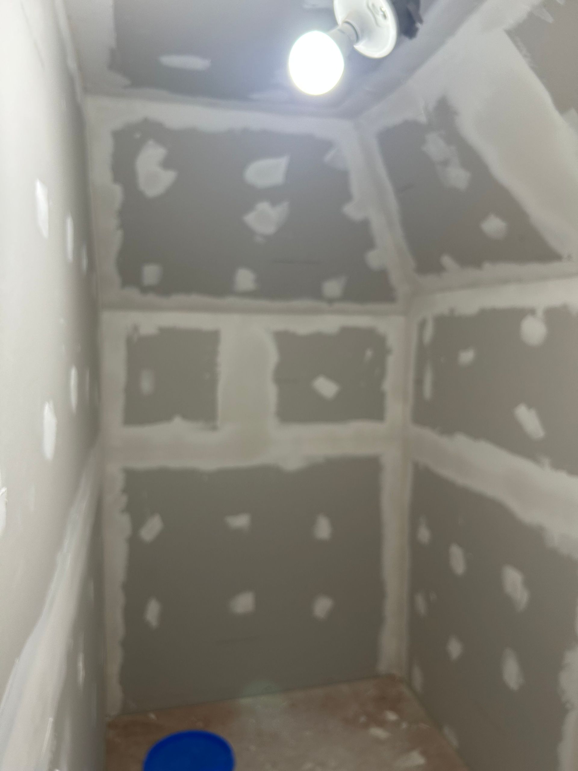 Interior of a small room with drywall and spackle, under construction, with a light fixture.