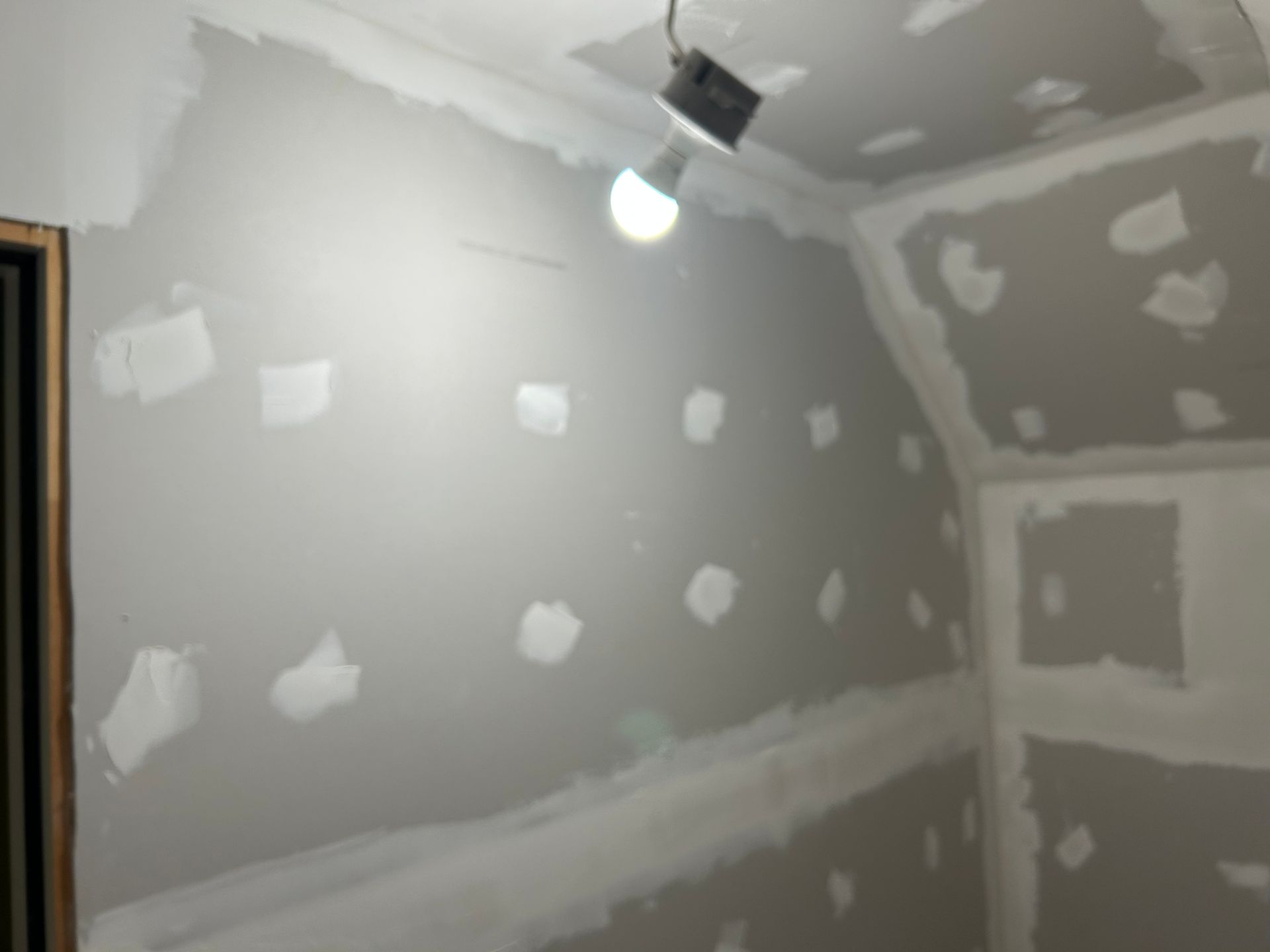 Interior room with drywall patches and unfinished walls. A lightbulb illuminates the space.