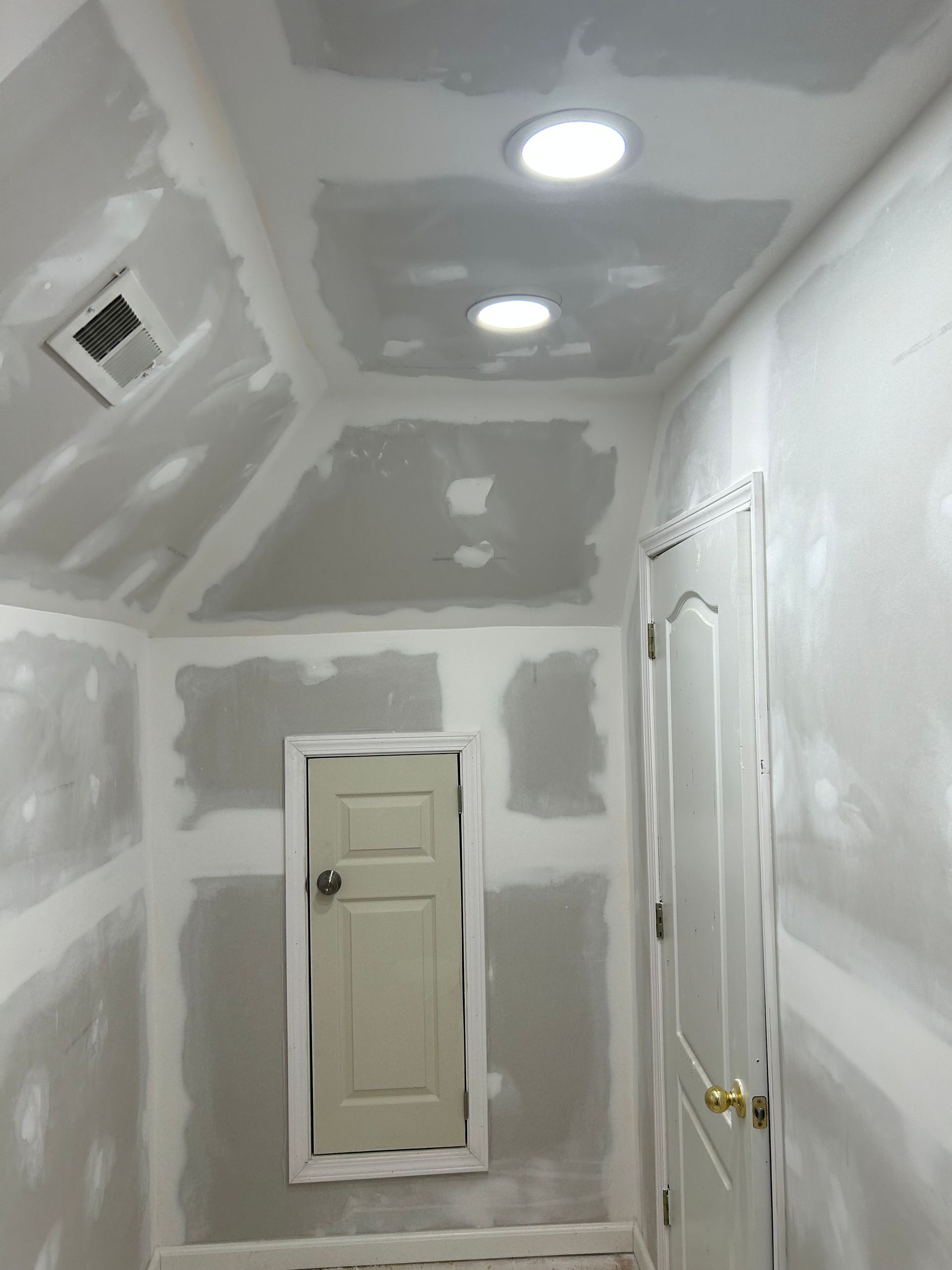 Room under construction; drywall walls and ceiling; small access door; recessed lights.