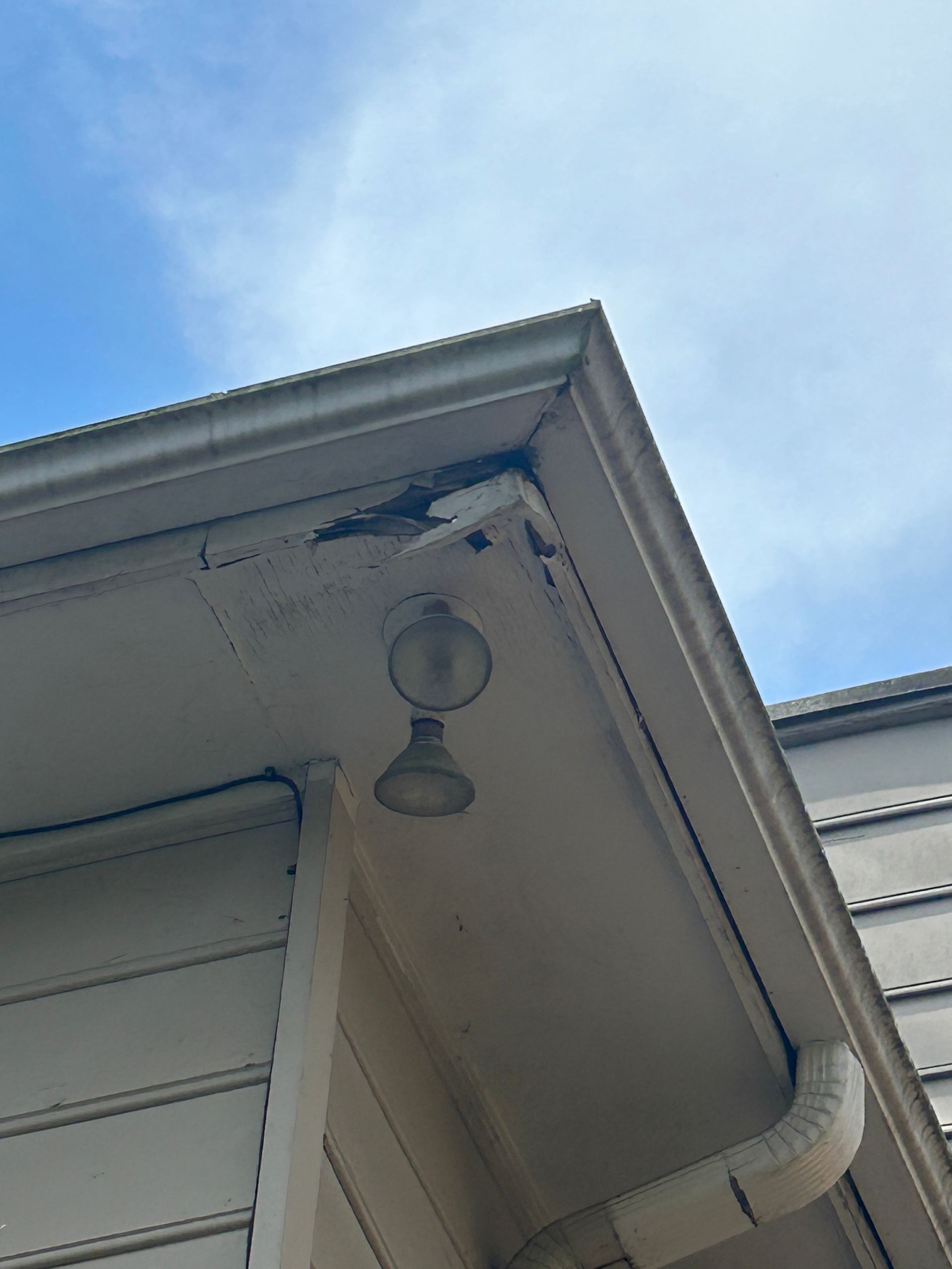 Corner of a house with white siding, gutter, and light fixture against a blue sky.
