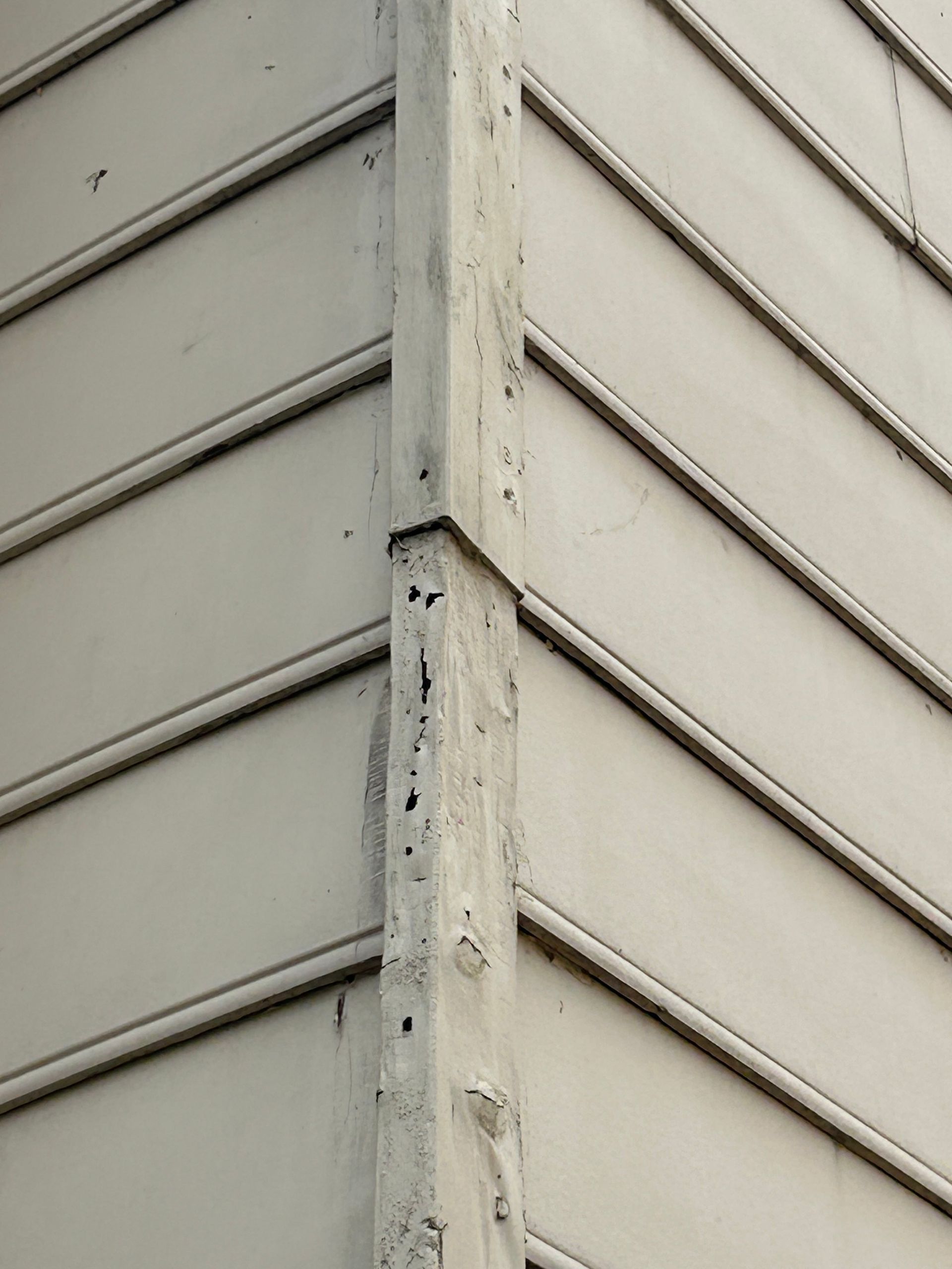 Corner of a building with pale siding, separated by a vertical column of wood painted the same color.