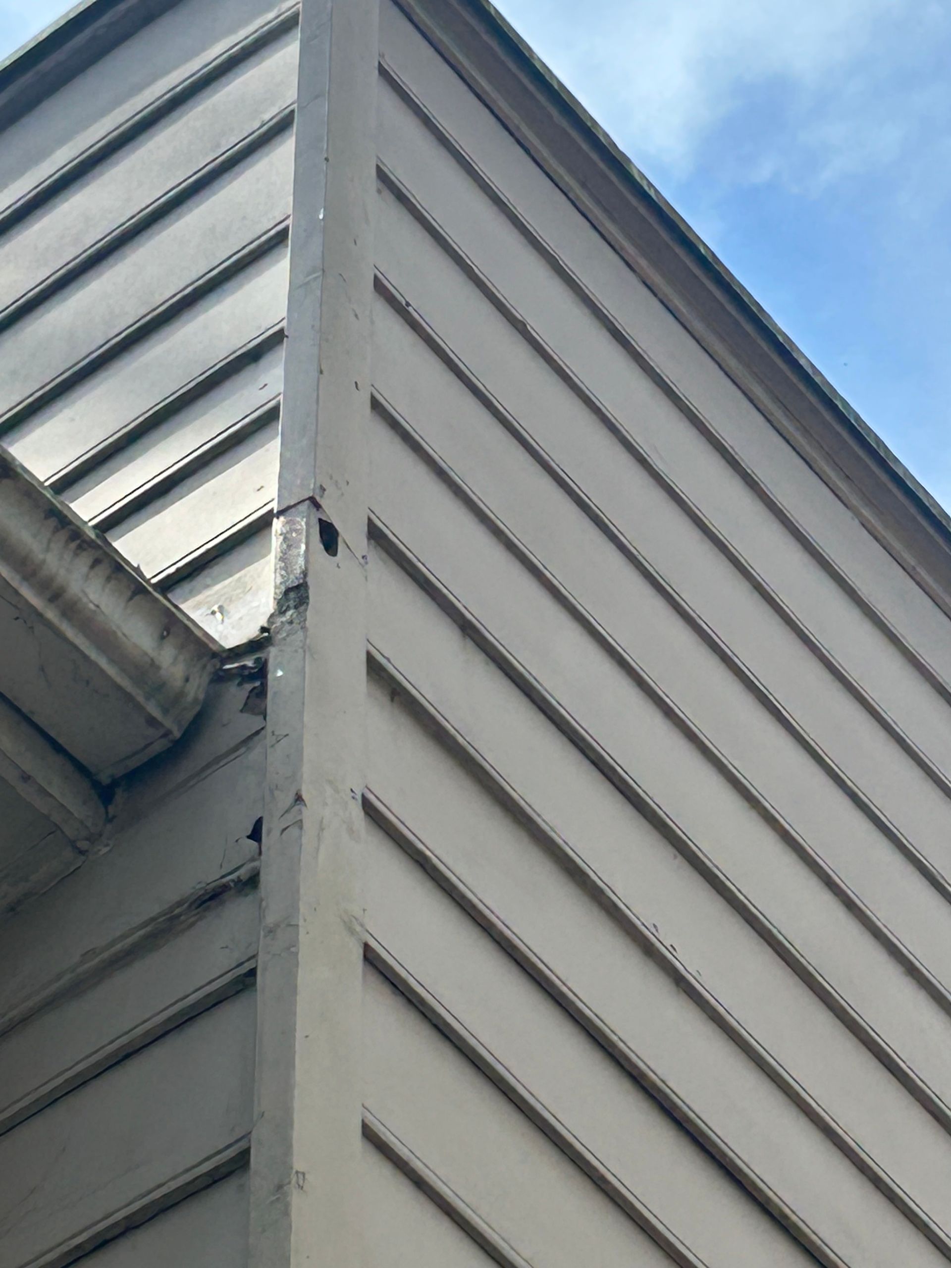 Beige siding and trim on a building corner with a blue sky in the background.