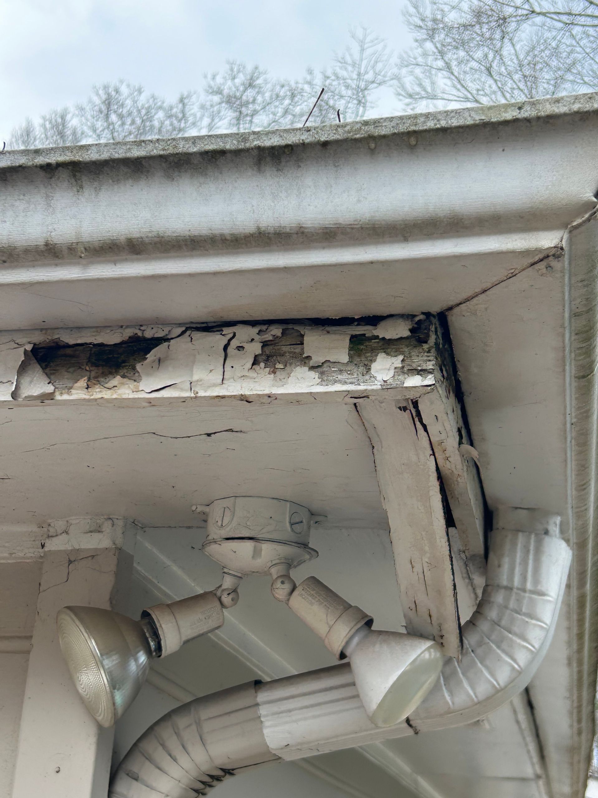 Overhead shot of deteriorating white building trim, with peeling paint and a security light.
