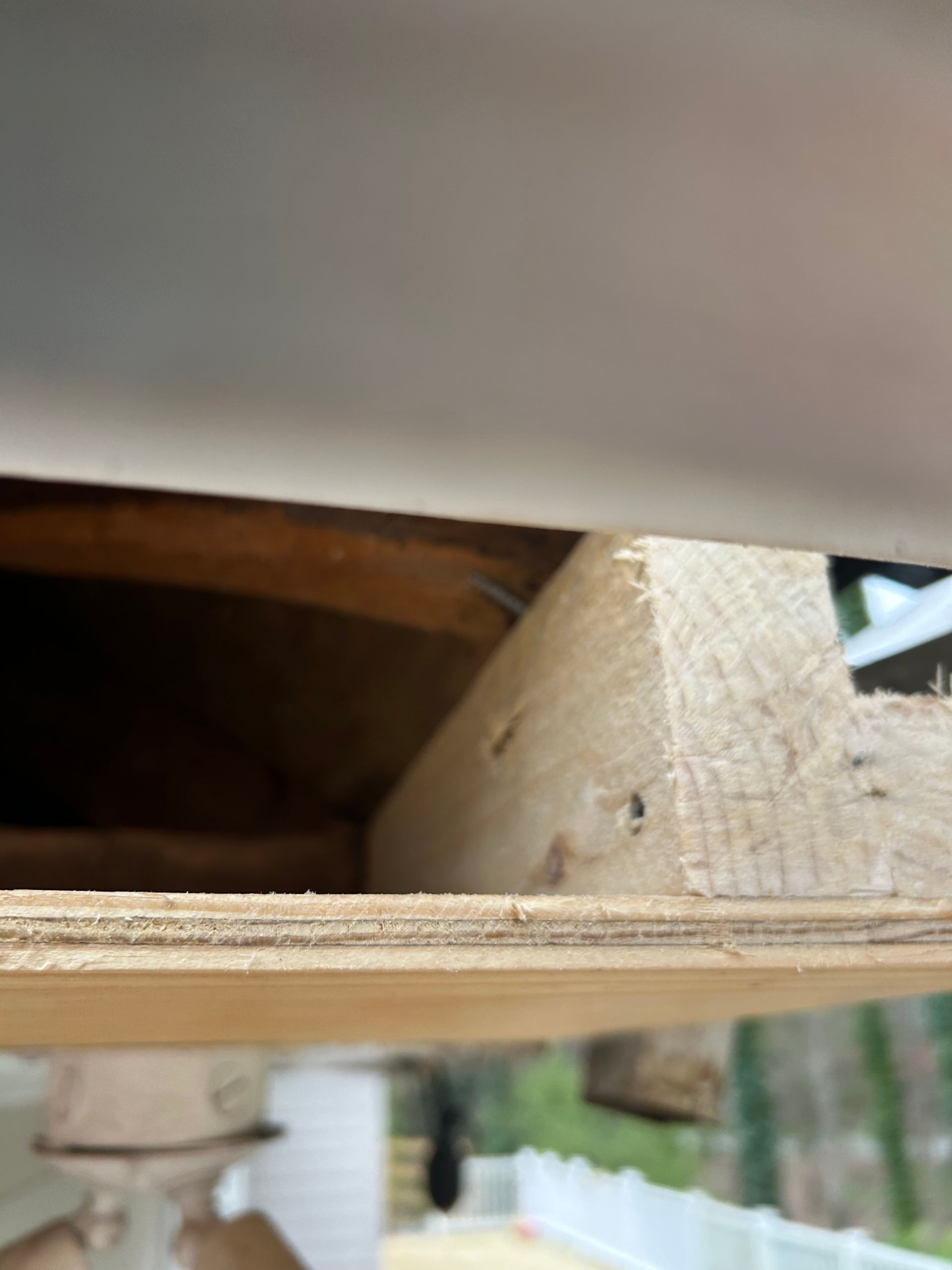 Close-up view of wood construction under a white trim, revealing nails and layered planks.