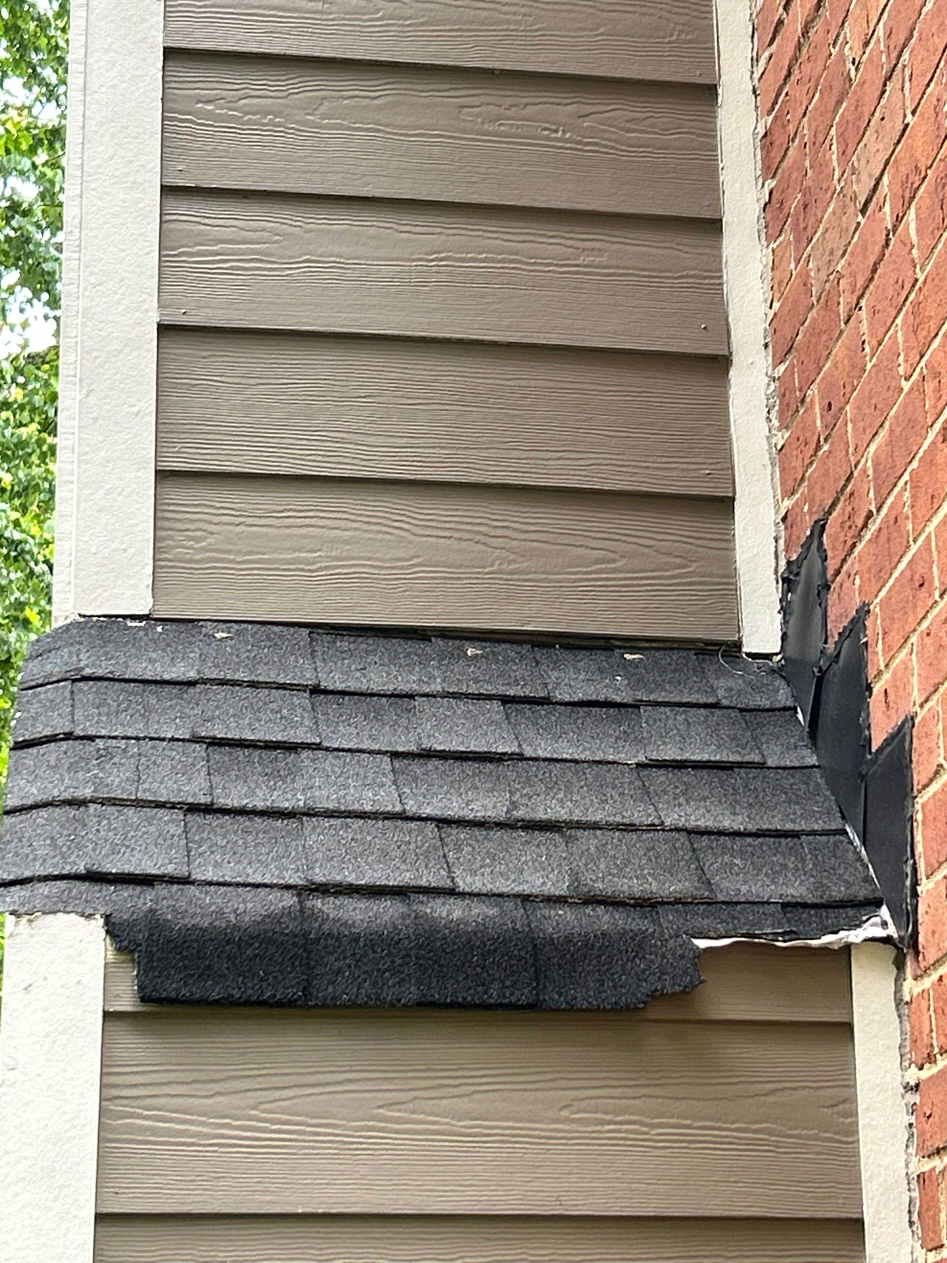 Section of house with brown siding, a black shingle section, and brick chimney.