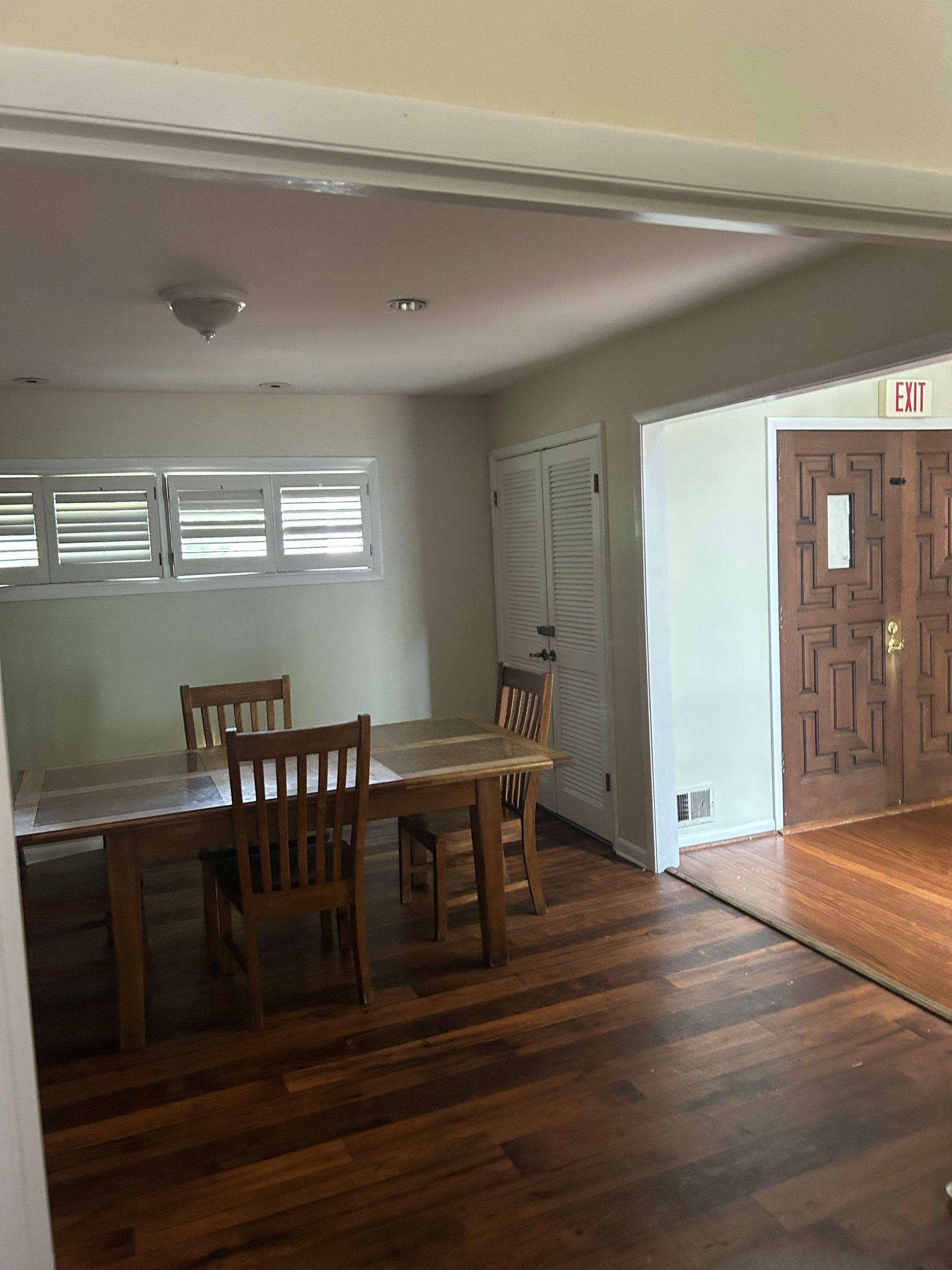 Dining room with wooden table, chairs, and floors. White walls, windows, and closed closet door.