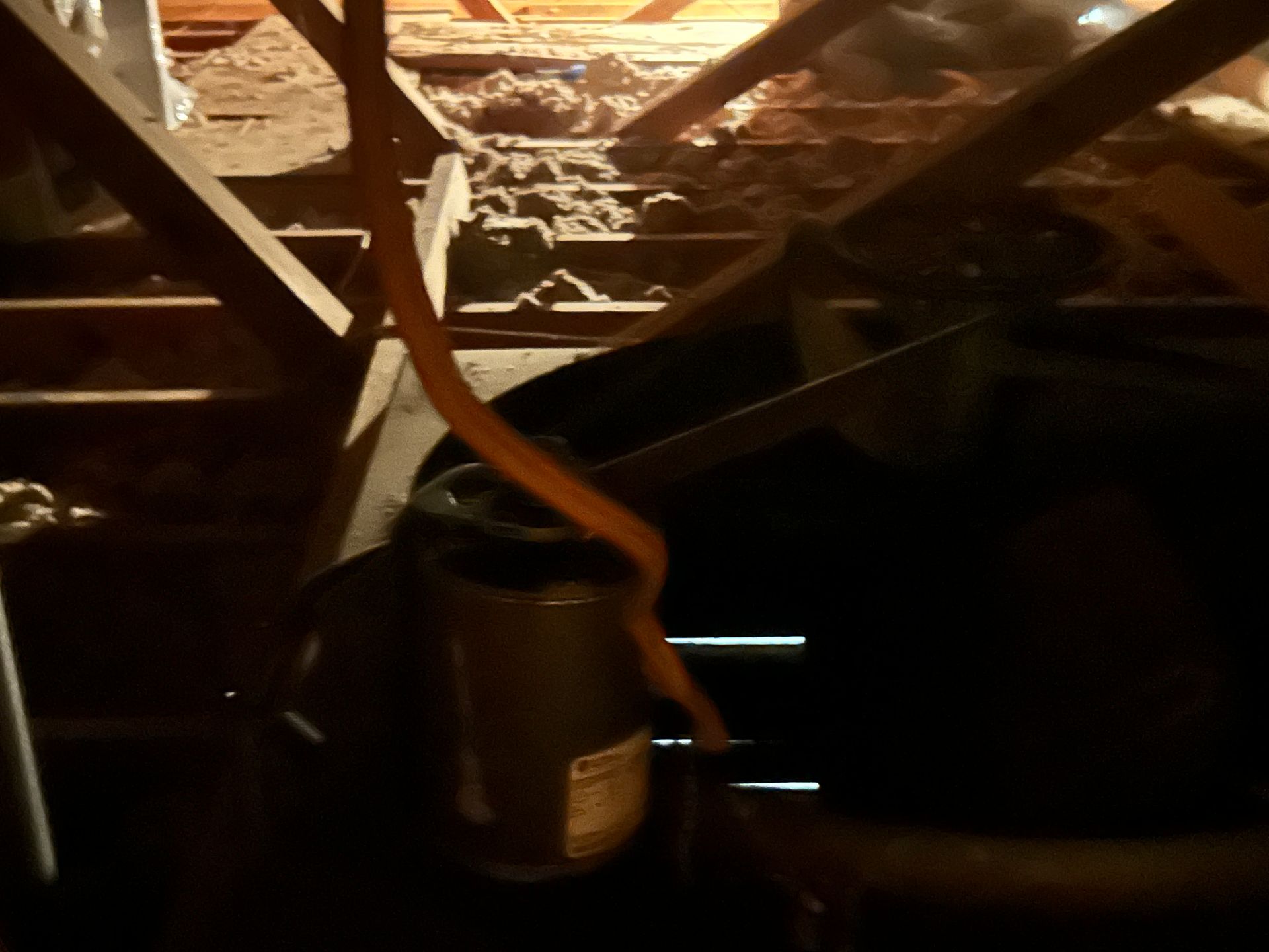 A dark attic with a cylindrical object and orange strap. Boards and insulation are visible.