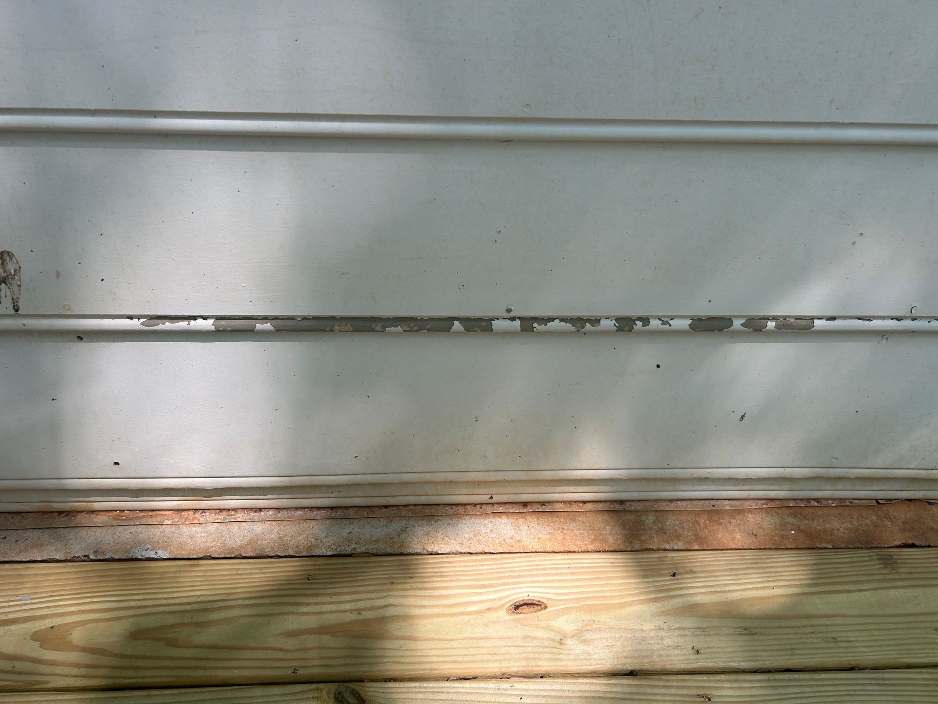 White siding with peeling paint above wooden deck.