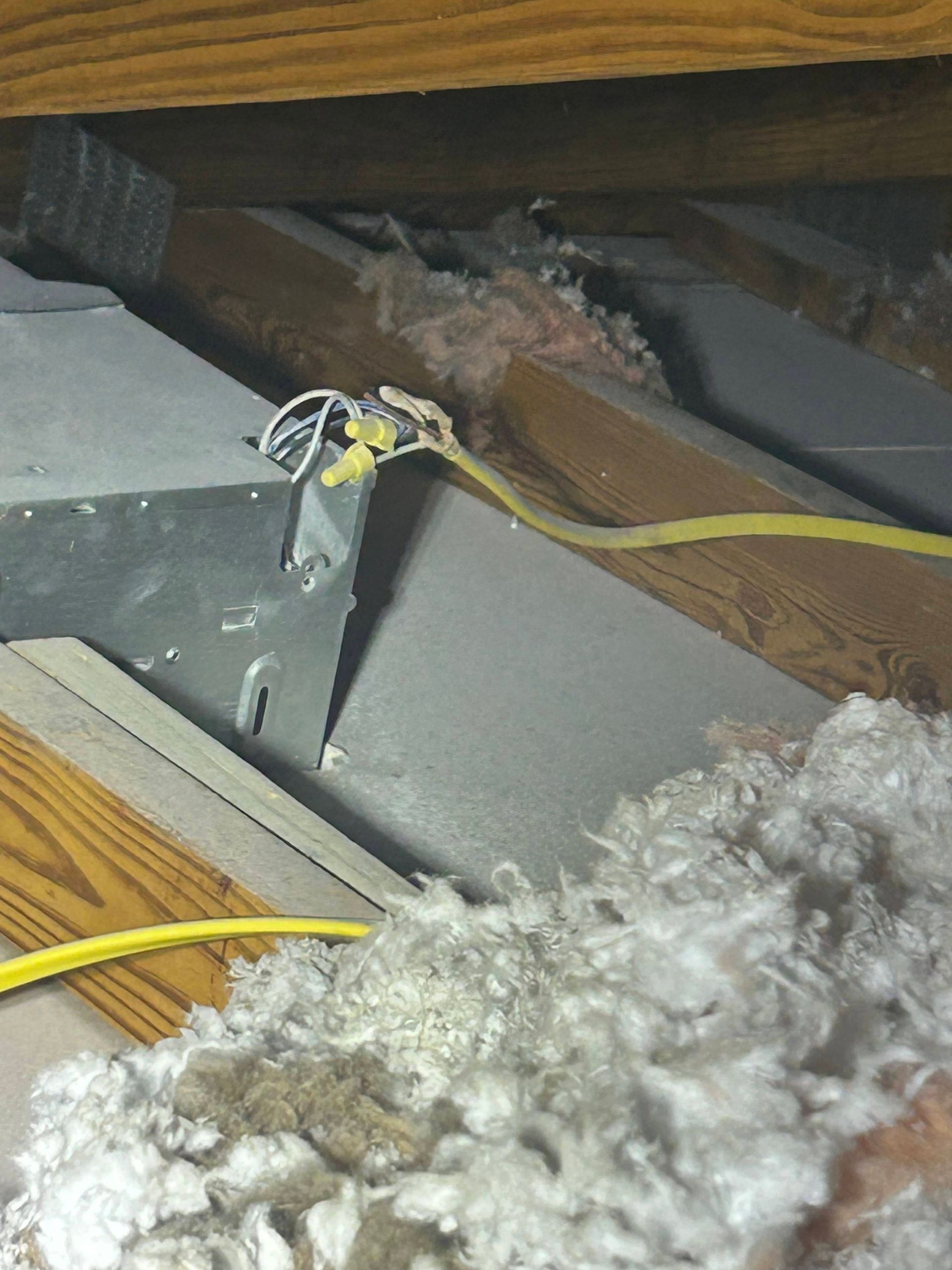 Electrical wires and ductwork in an attic, surrounded by insulation and wooden beams.