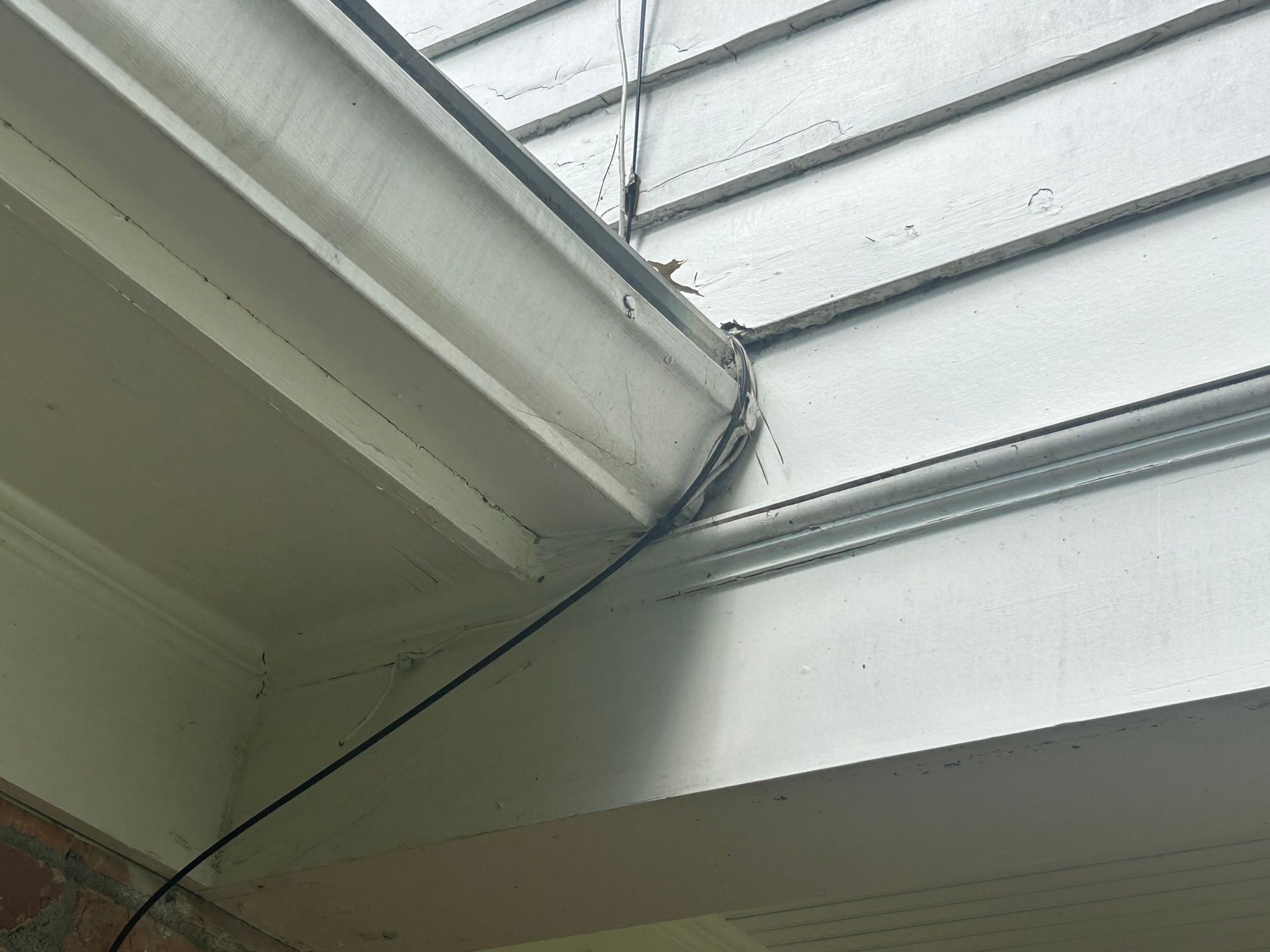 Black cable running across white house trim and gutter.