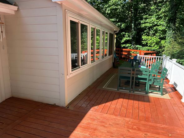Red wooden deck next to a sunroom with windows. Green chairs surround a table.