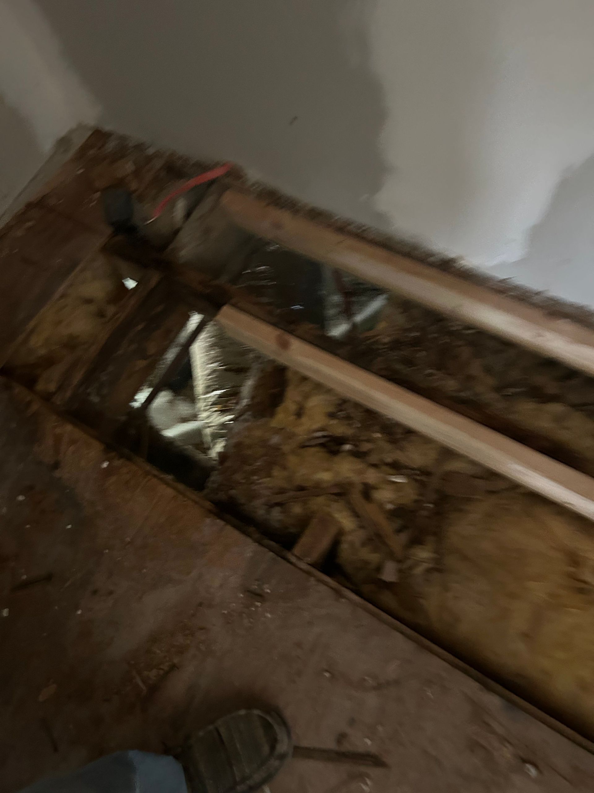 Opening in floor with exposed insulation and pipes. Wooden beams and wiring are visible.