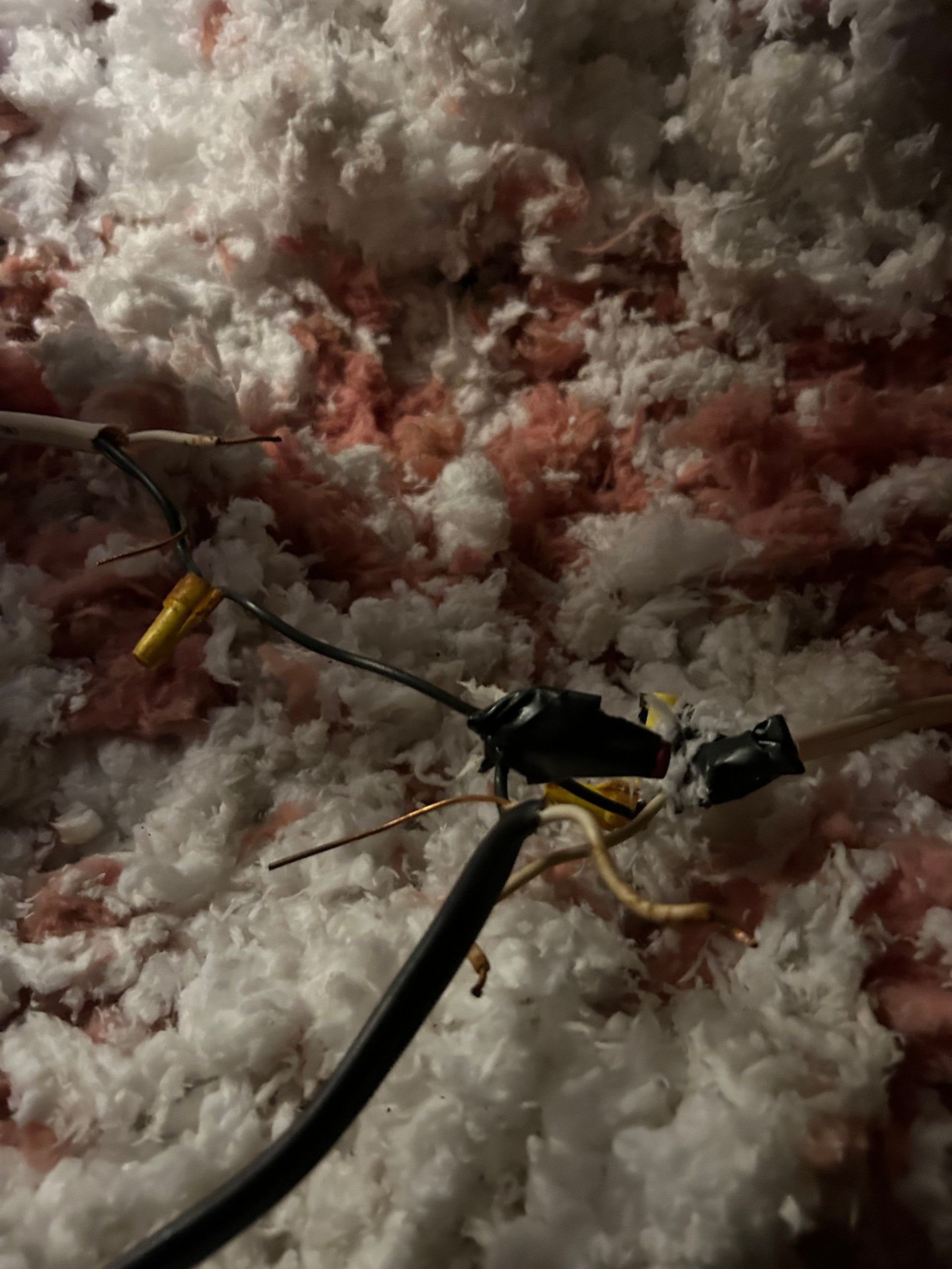 Electrical wires with wire connectors amidst pink and white insulation in an attic.