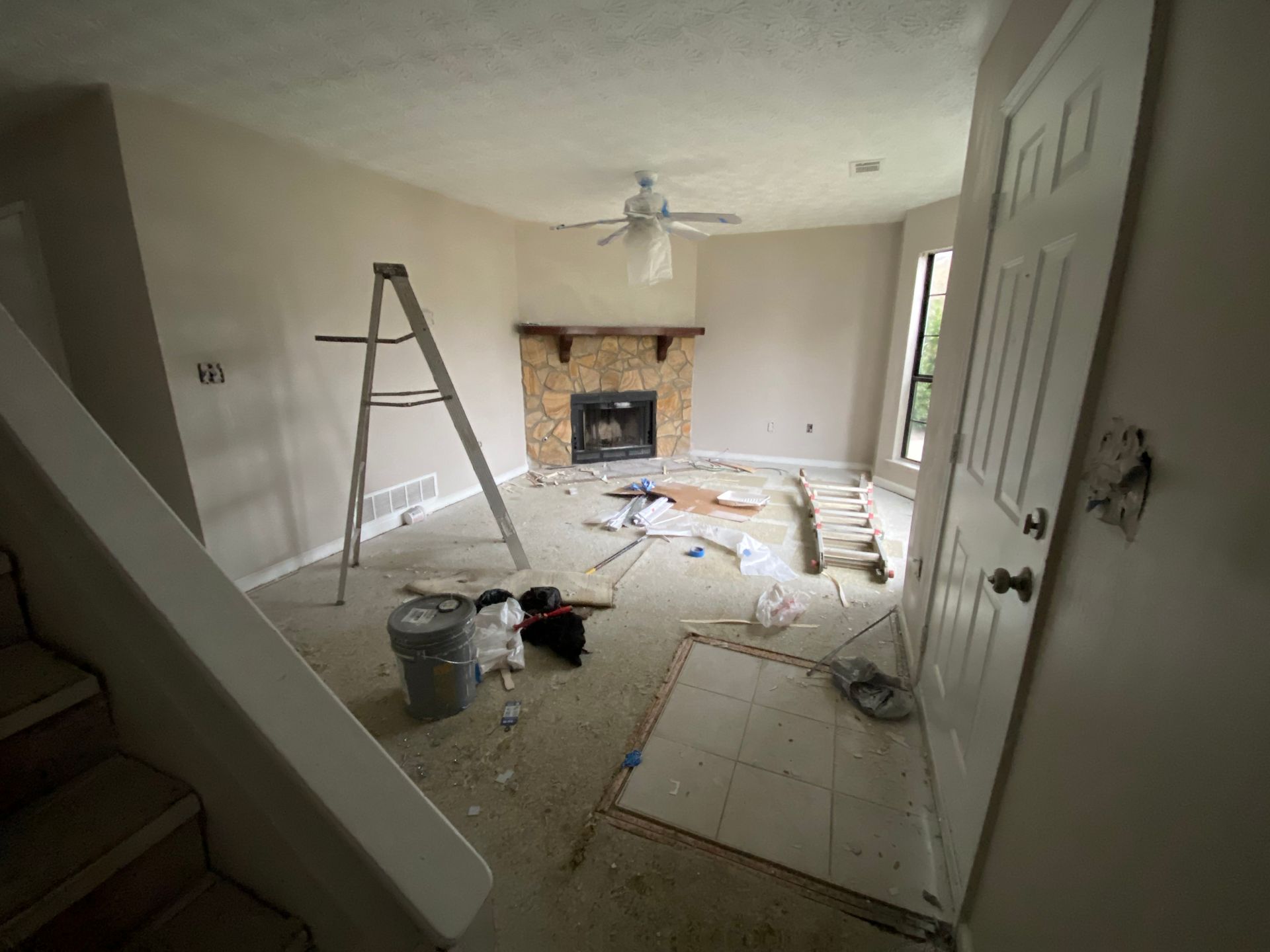 Living room under renovation with a fireplace, ladder, and exposed flooring.