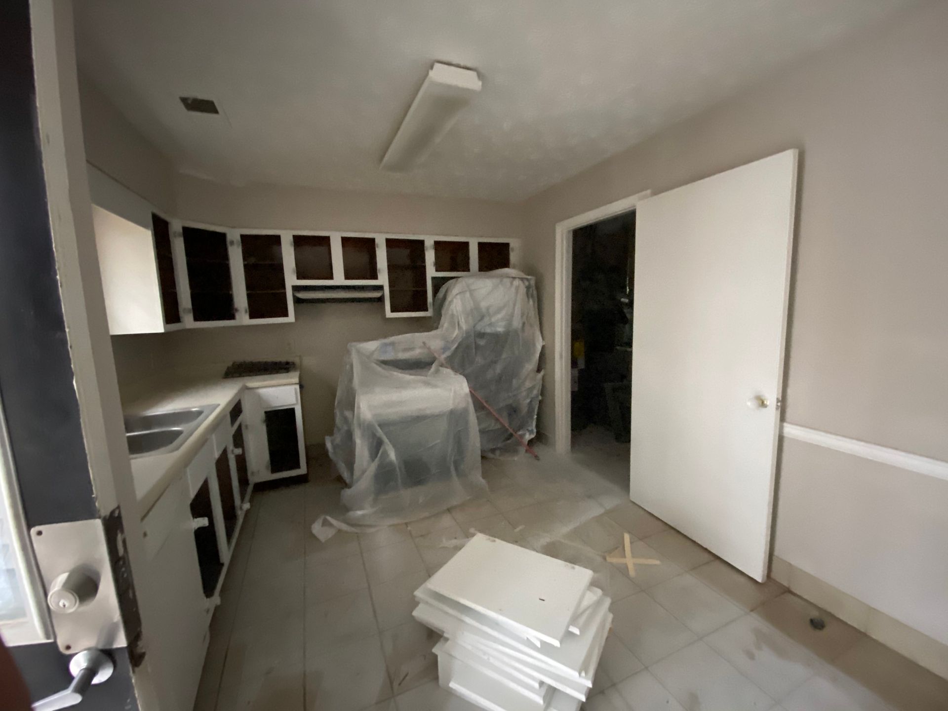 Kitchen under renovation, cabinets open, stove covered, paint materials visible.