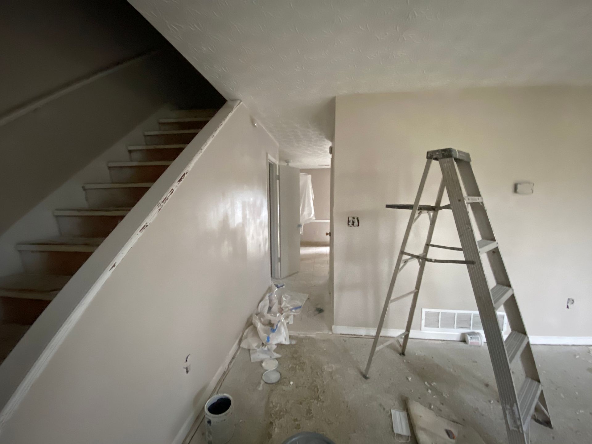 A room under renovation with stairs, ladder, and freshly painted walls in neutral tones.