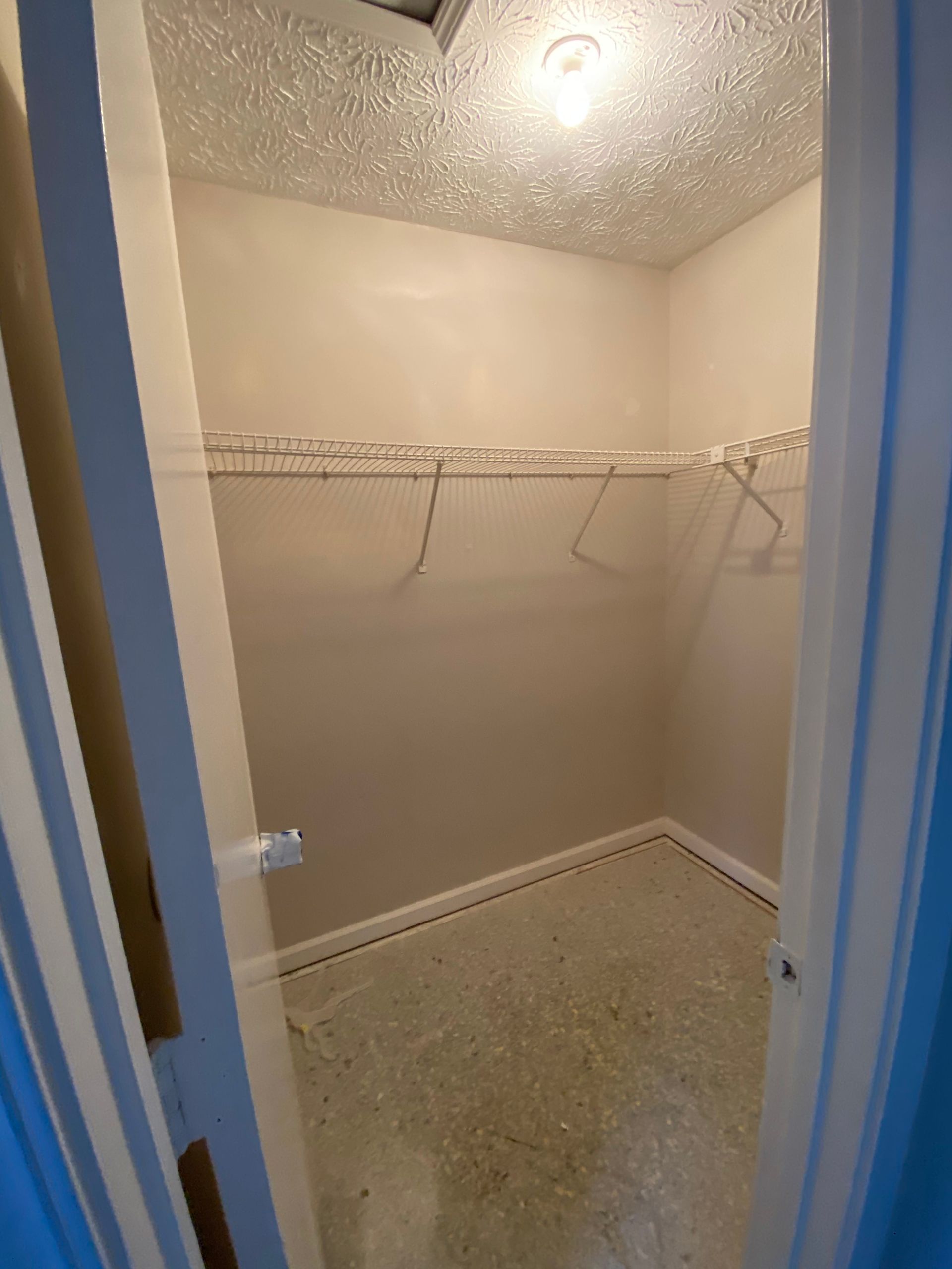 Empty walk-in closet with wire shelving, tan walls, and a textured ceiling.