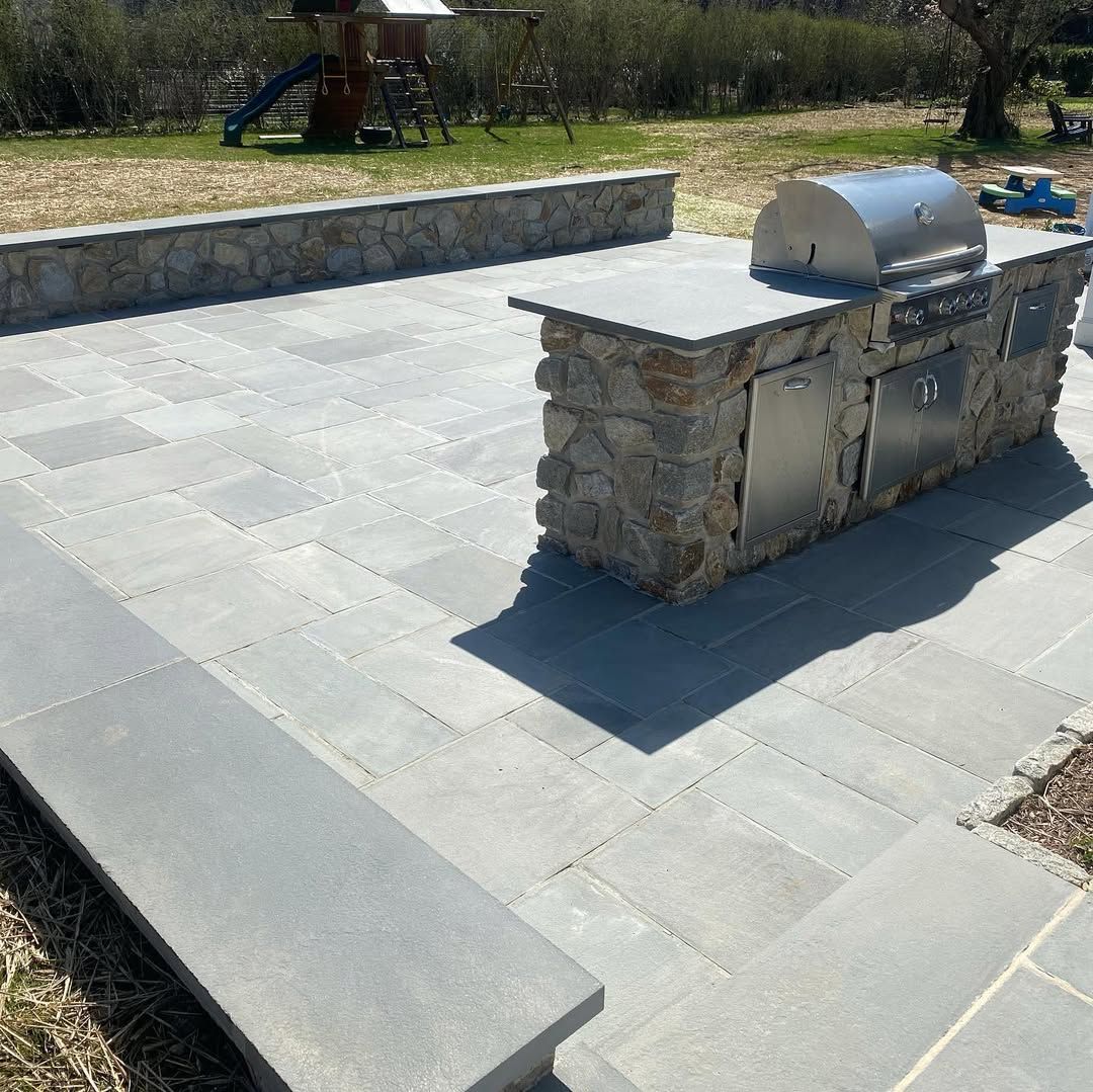 A patio with a grill and a stone wall