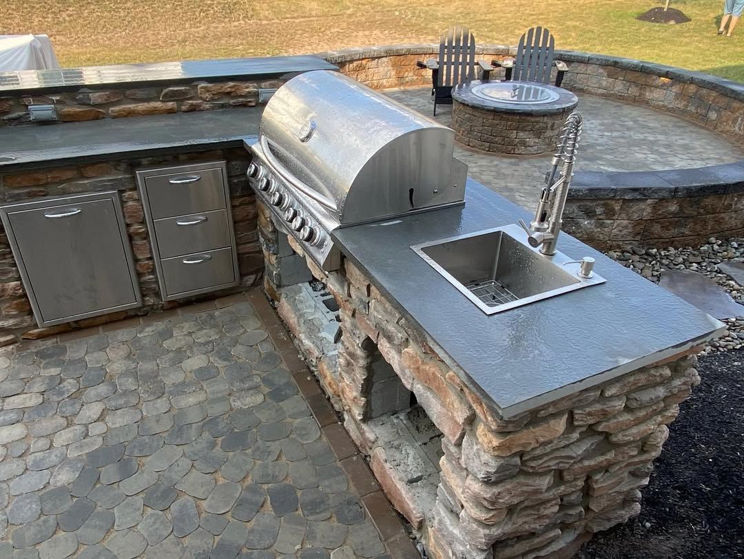 An outdoor kitchen with a grill , sink and fire pit.