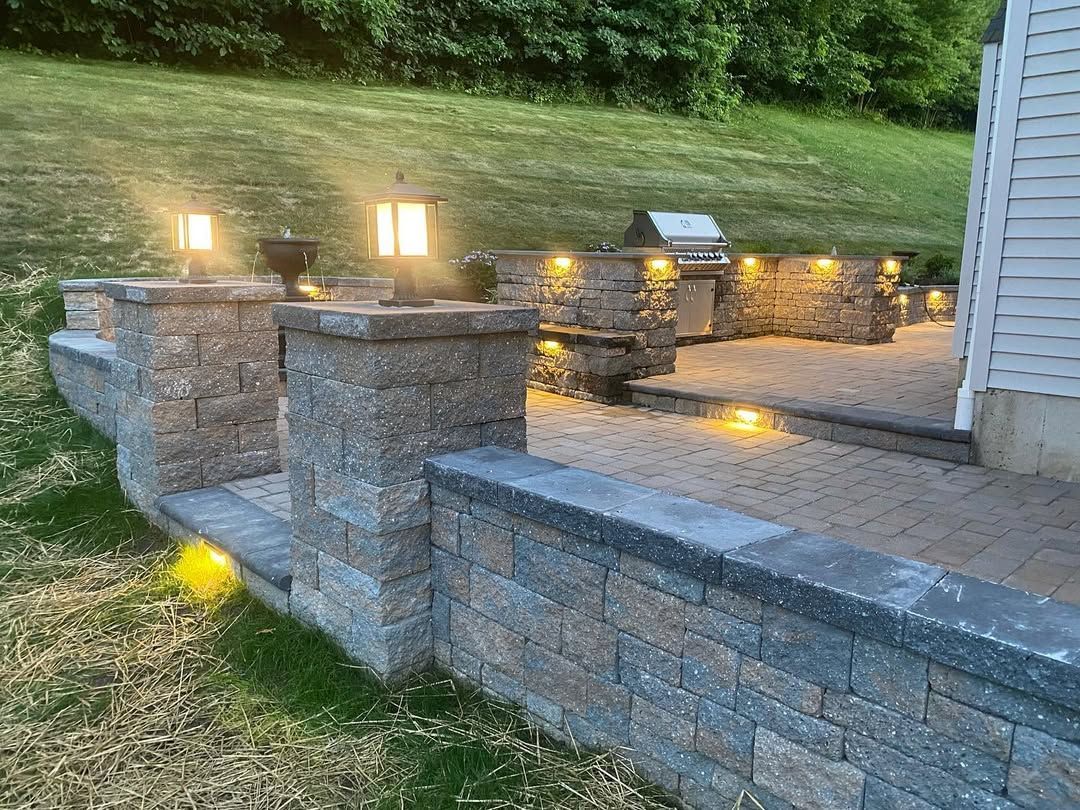 A brick wall with lights on it and a grill in the backyard.