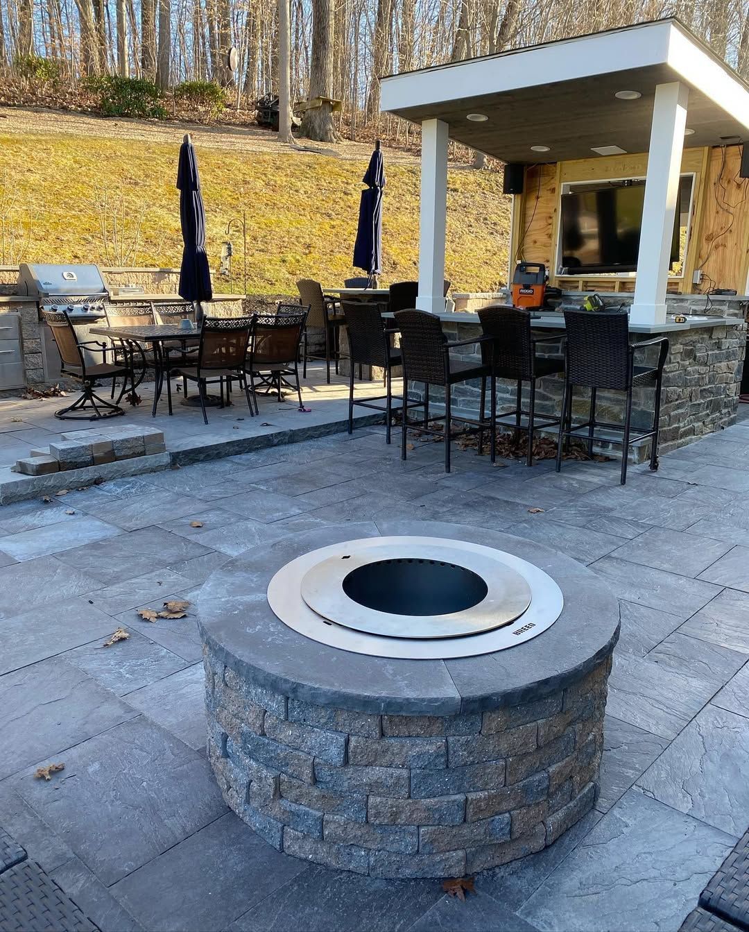 A fire pit is in the middle of a patio with tables and chairs.