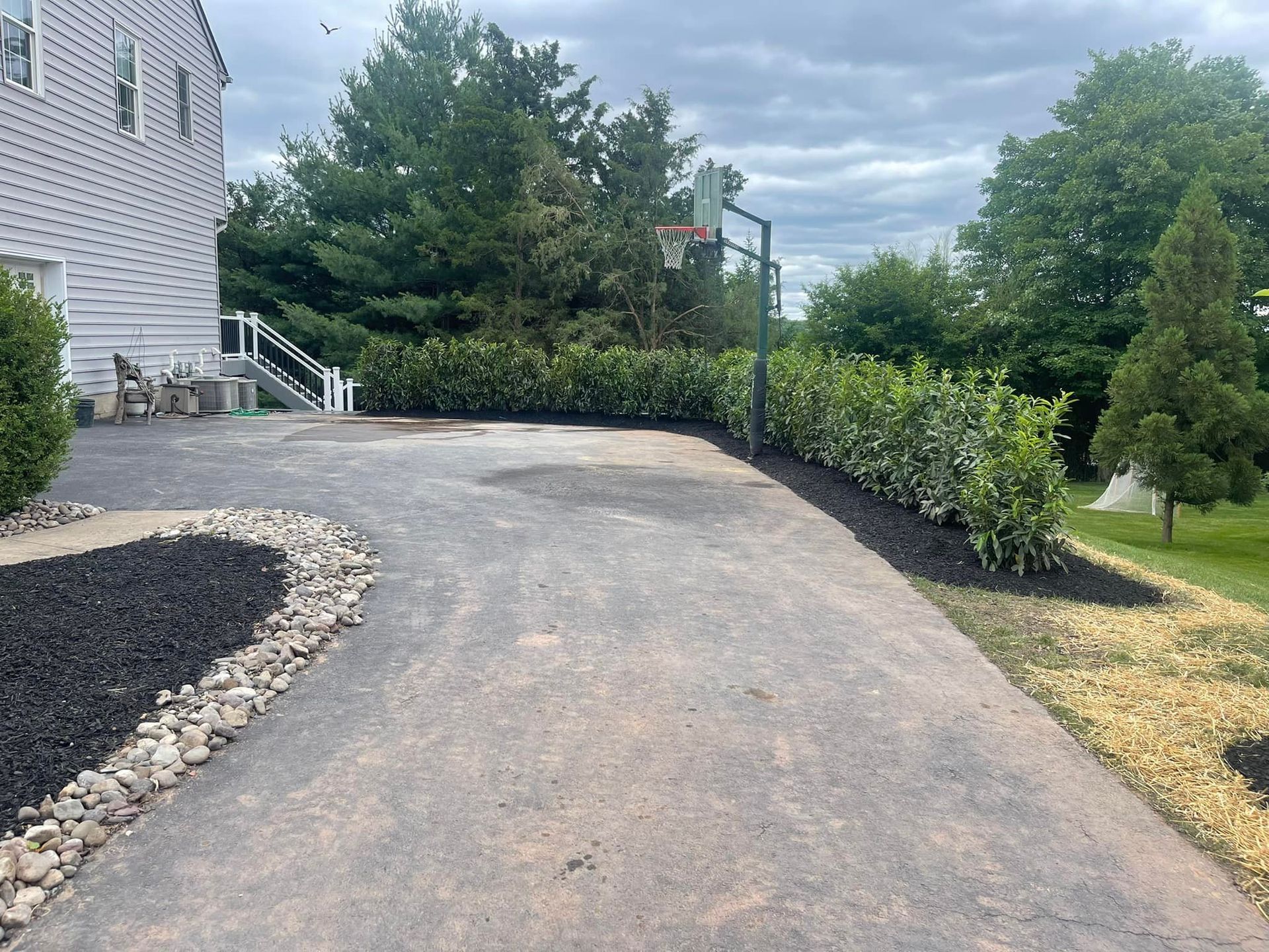 A driveway leading to a house with a basketball hoop in the backyard.