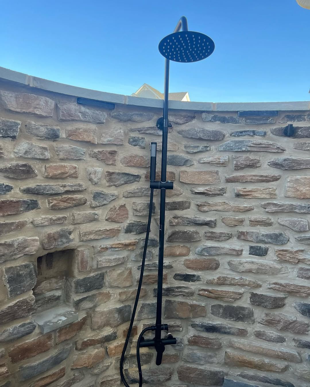A black shower head is hanging from a stone wall.