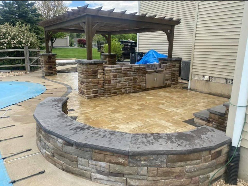 A patio with a pergola and a brick wall next to a pool.