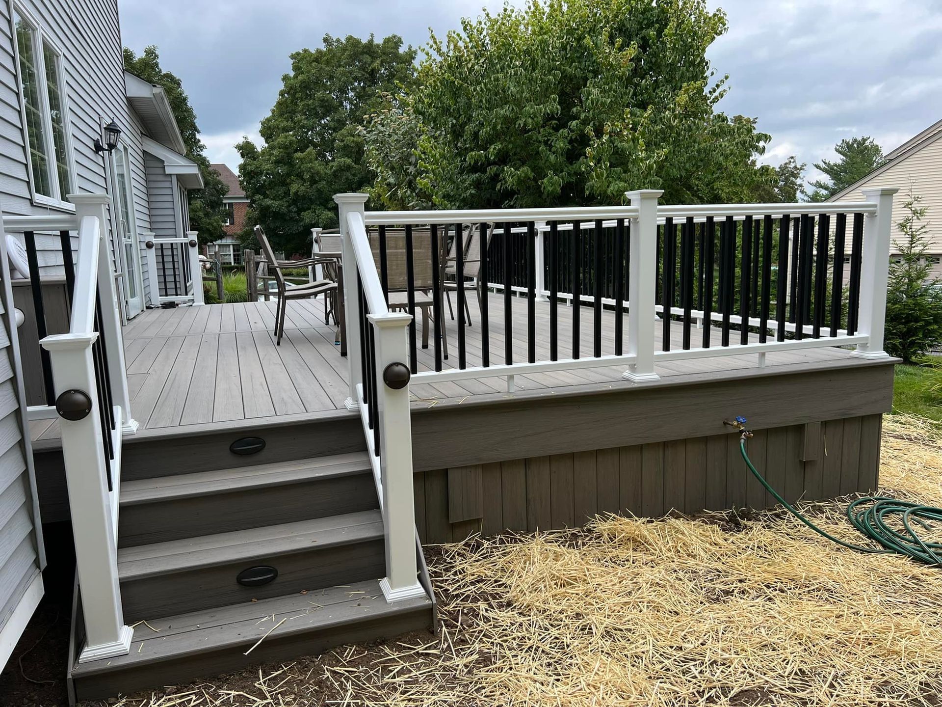 A deck with stairs and a white railing is in the backyard of a house.