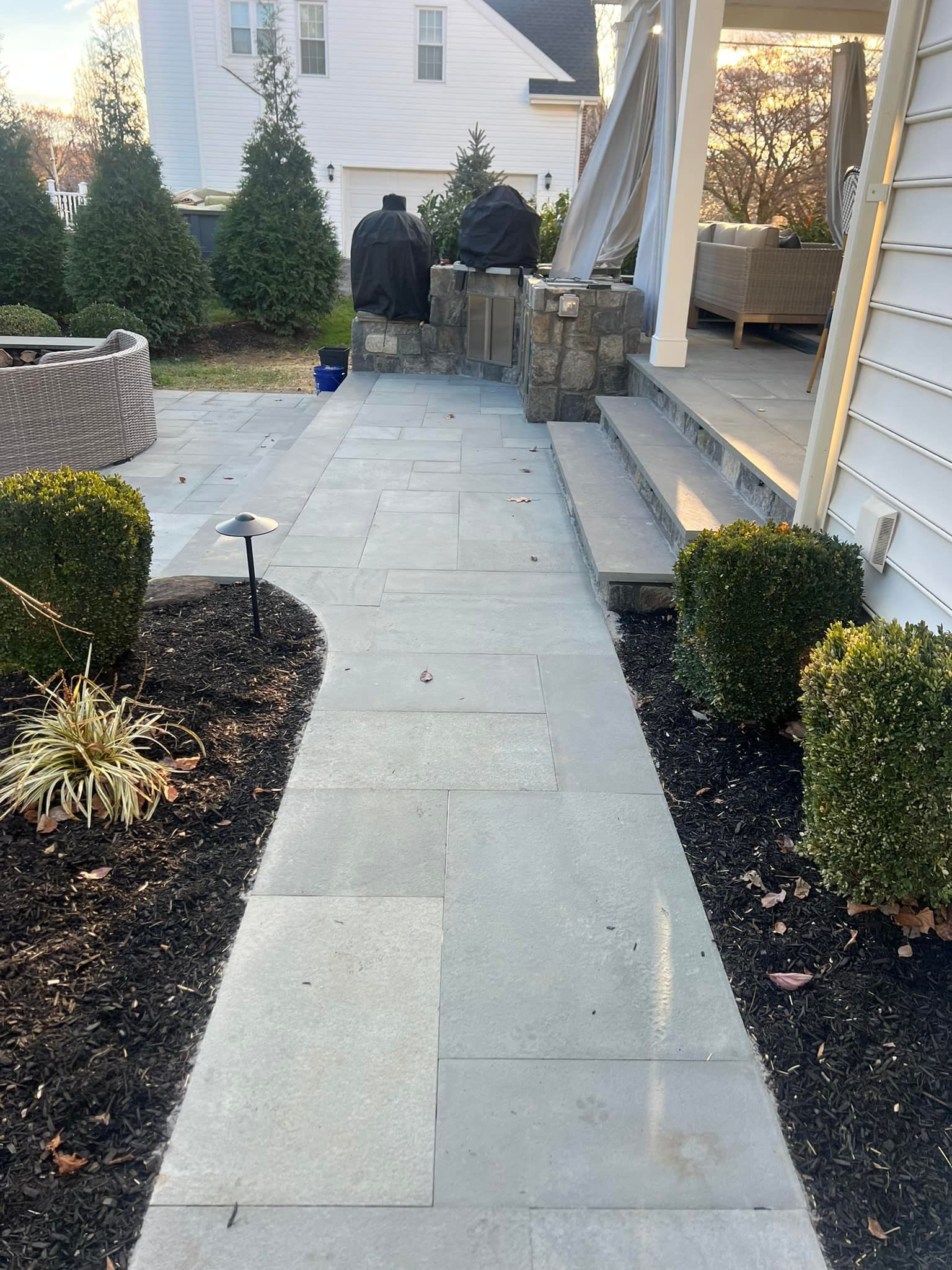 A walkway leading to a patio with a grill and a house in the background.