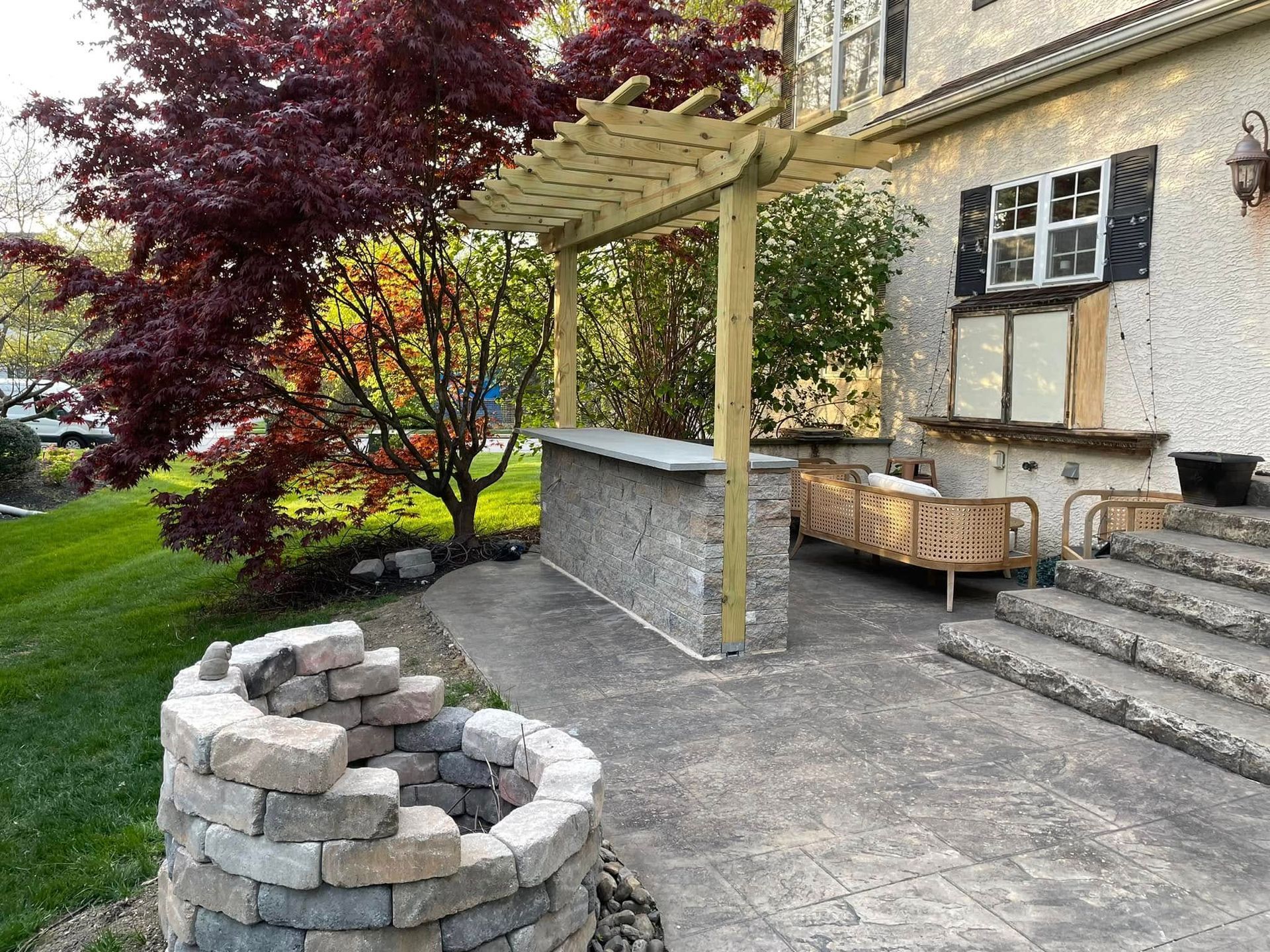 A patio with a fire pit and a pergola in front of a house.