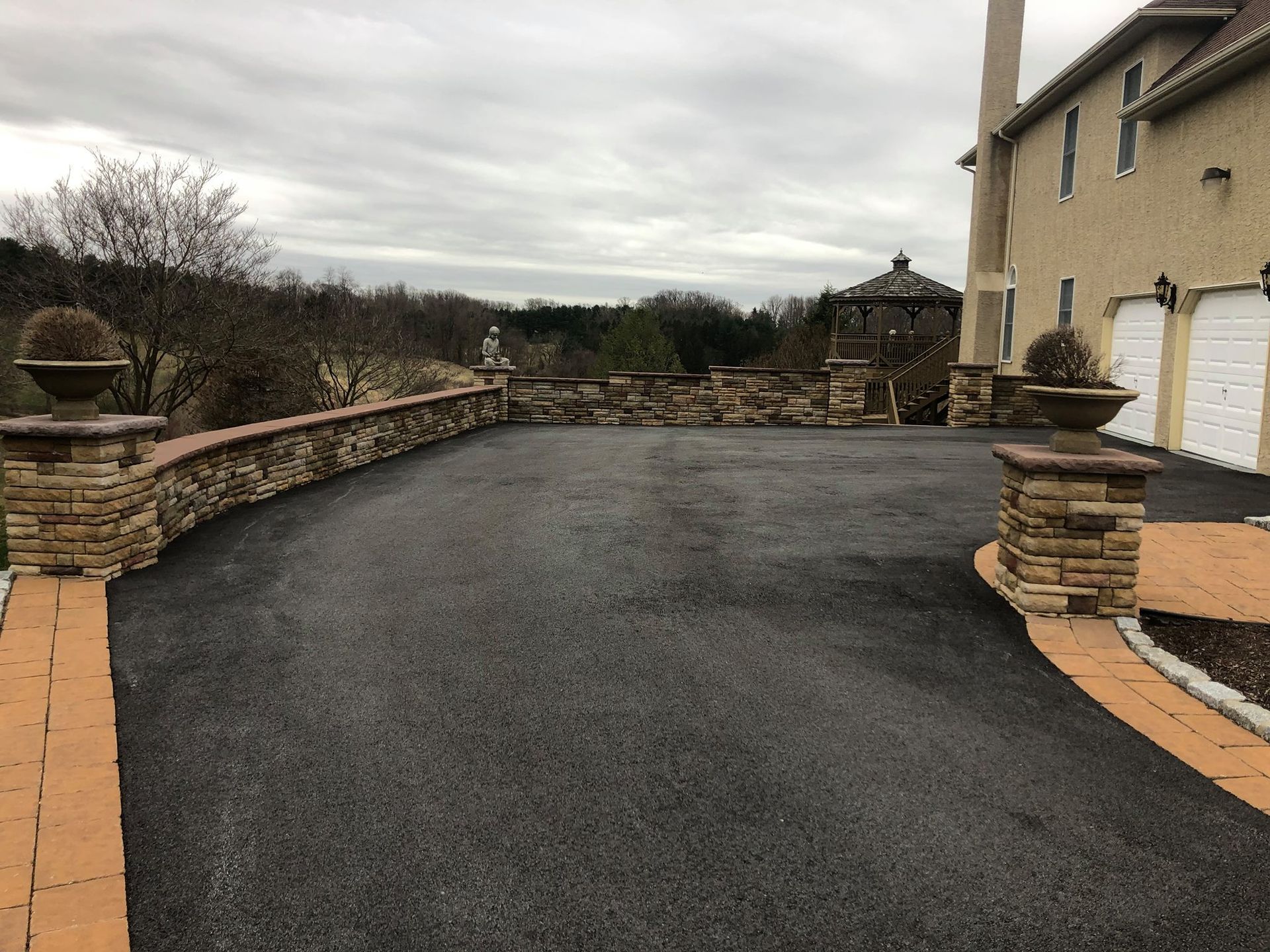 A driveway leading to a large house with a stone wall.