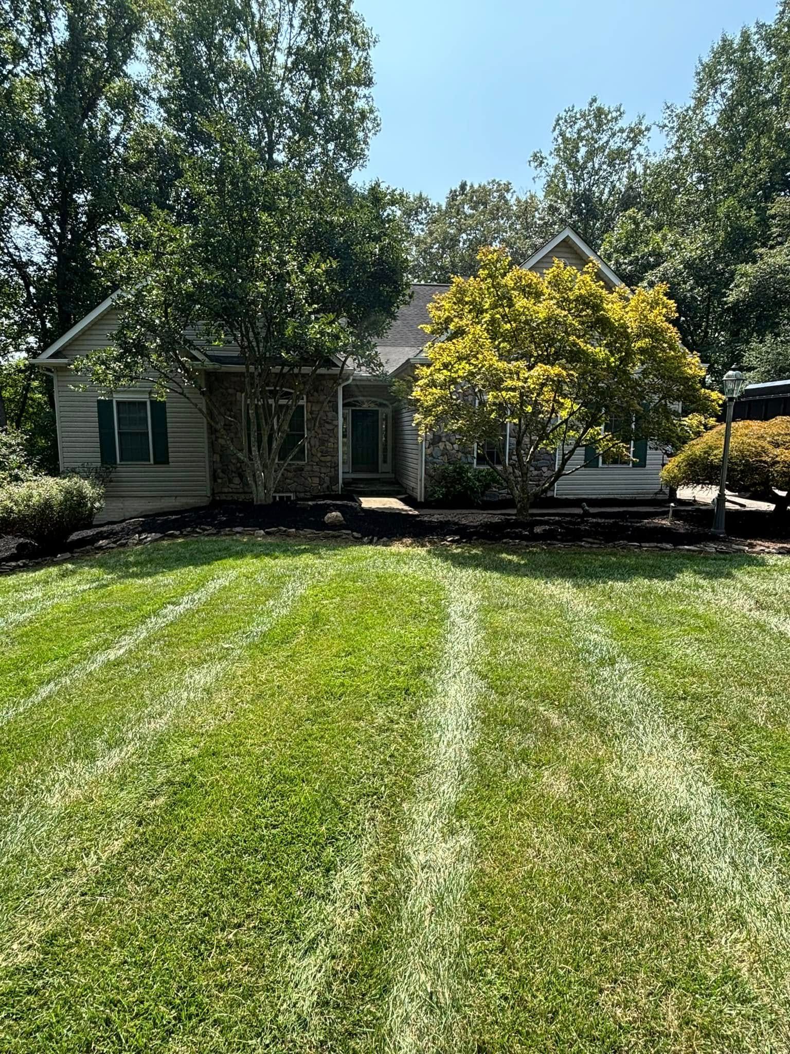 A one-story home with a stone-accented facade, green shutters, and a lawn with fresh mowing lines, surrounded by trees.