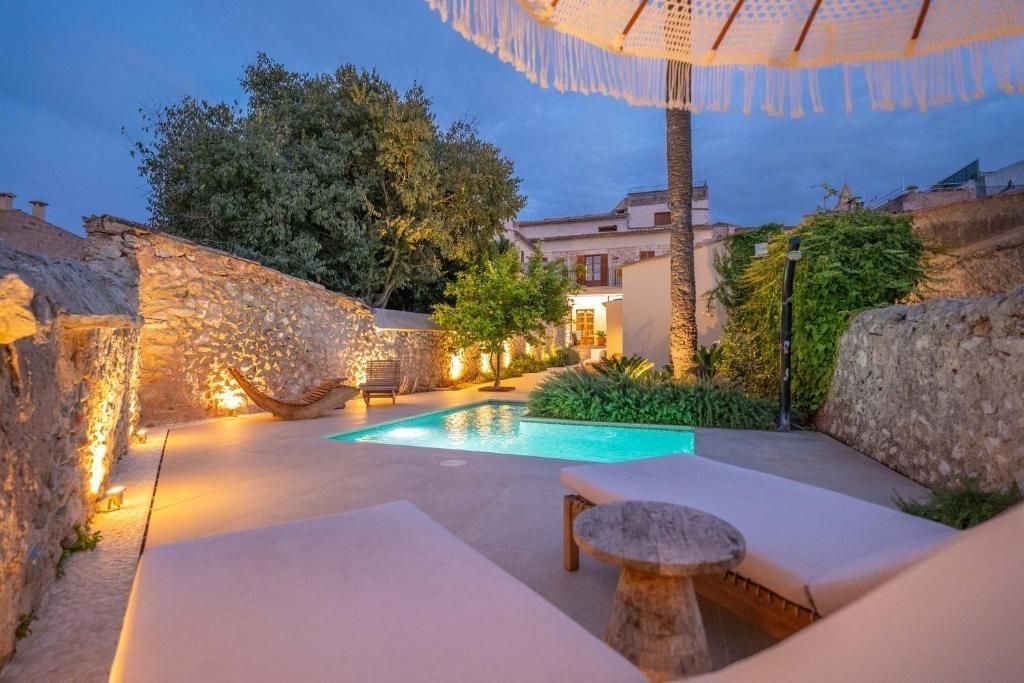 Zona de descanso junto a la piscina al atardecer. Tumbonas, muros de piedra, sombrilla, piscina pequeña y árboles.